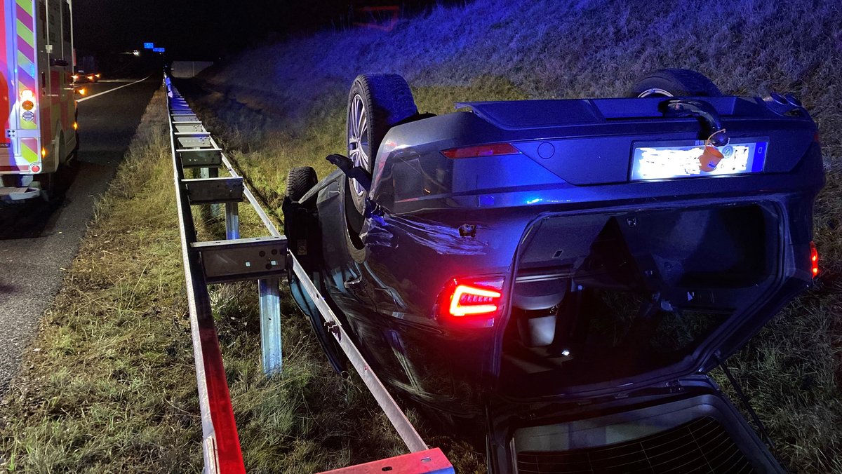 Ein Auto liegt auf der Autobahn hinter der Leitplanke auf dem Dach im Straßengraben.