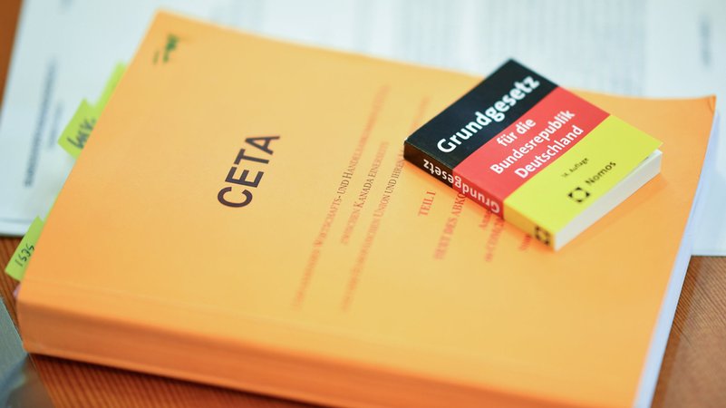 Zwei Bücher mit der Aufschrift "CETA" und "Grundgesetz" liegen vor Verhandlungsbeginn im Verhandlungssaal des Gerichts.