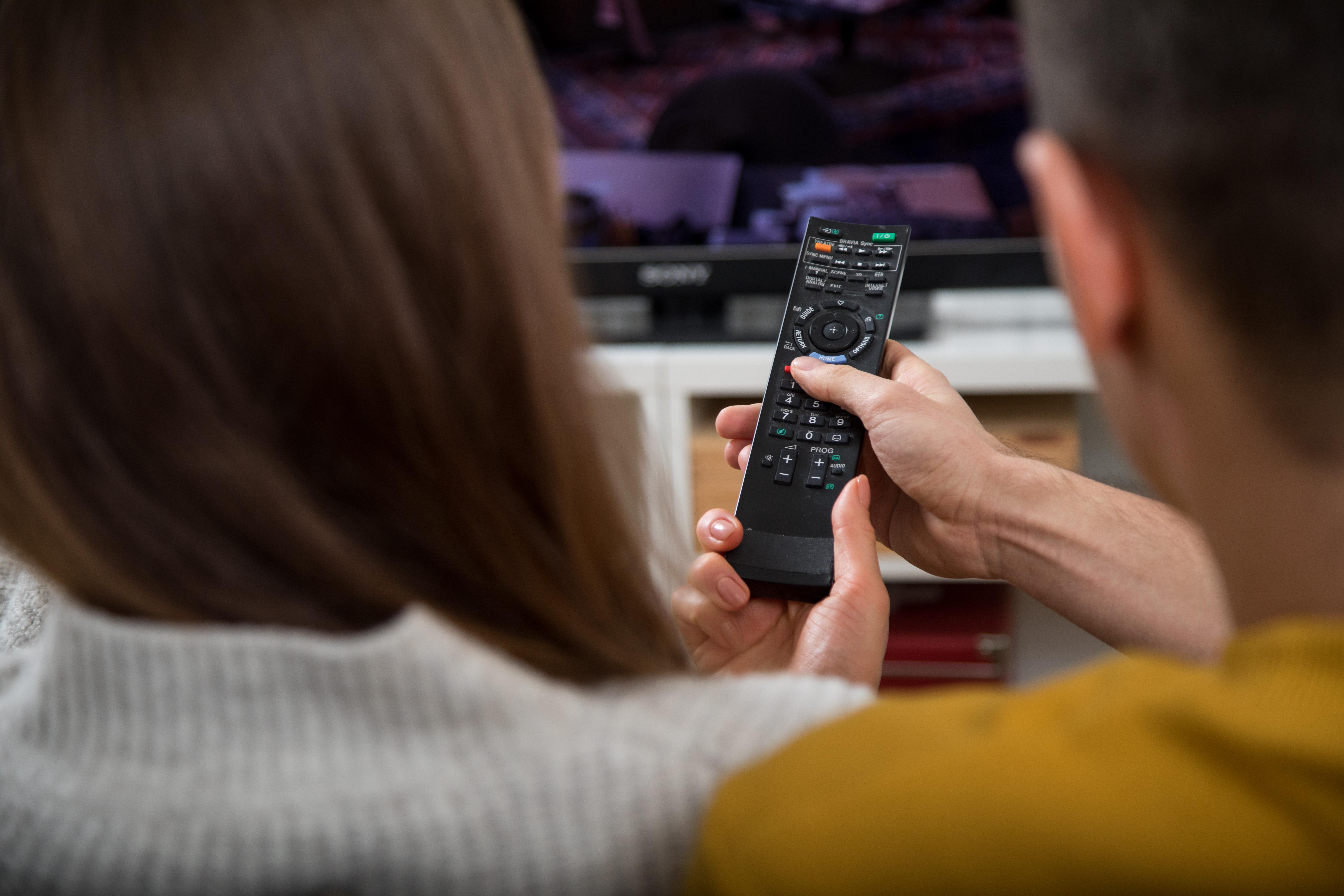 Mann und Frau auf einem Sofa bedienen einen Smart-TV per Fernbedienung.