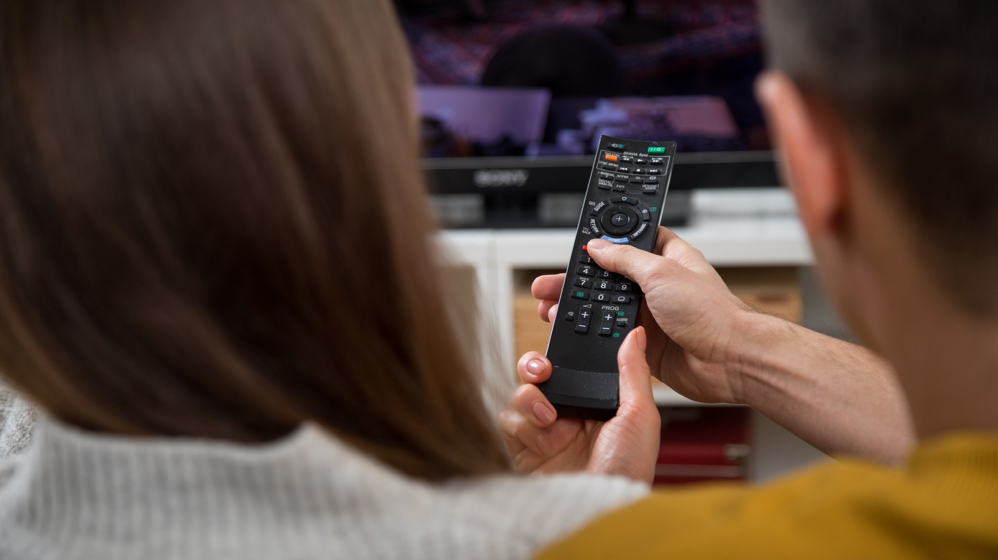 Mann und Frau auf einem Sofa bedienen einen Smart-TV per Fernbedienung.