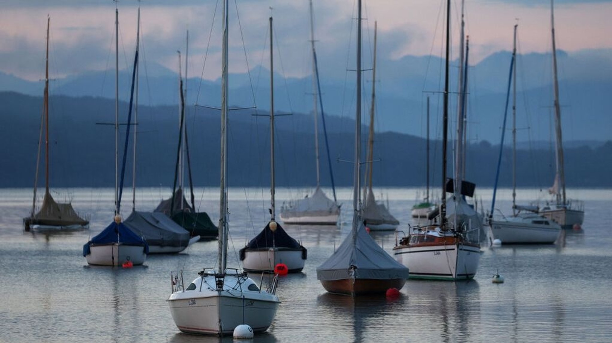 Segelboote liegen im Sonnenaufgang vor dem Panorama der Alpen auf dem Ammersee. 