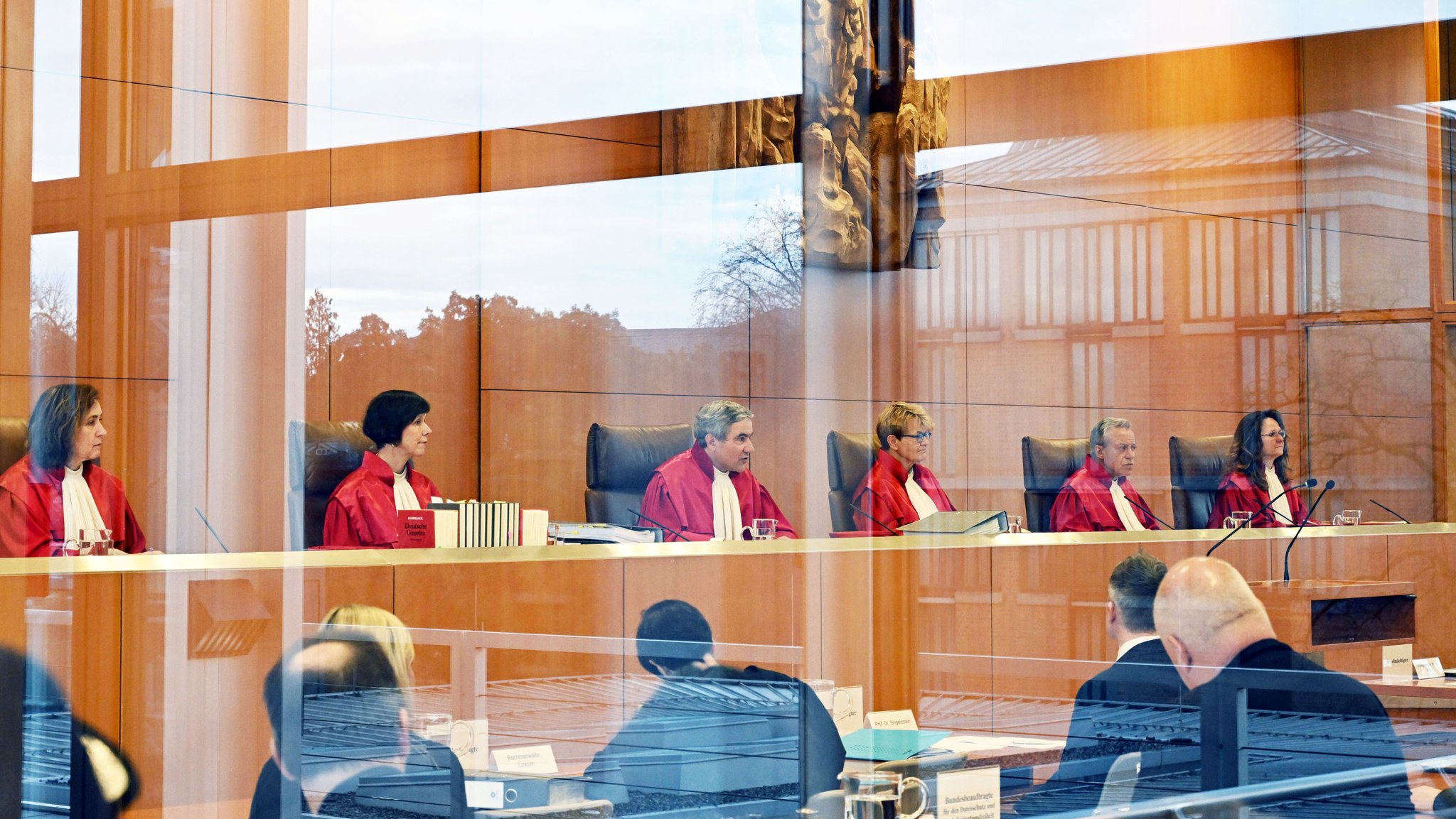 Der Erste Senat des Bundesverfassungsgerichts , (l-r) Yvonne Ott, Gabriele Britz, Stephan Harbarth, Vorsitzender des Senats und Präsident des Gerichts, Susanne Baer, Josef Christ und Ines Härtel, eröffnet die Verhandlung zu weitgehender Datenanalyse bei der Polizei (durch eine Scheibe fotografiert). Es geht dabei um neue Ermittlungsmethoden der Polizei per automatisierter Datenauswertung. (Archiv: 20.12.2022)