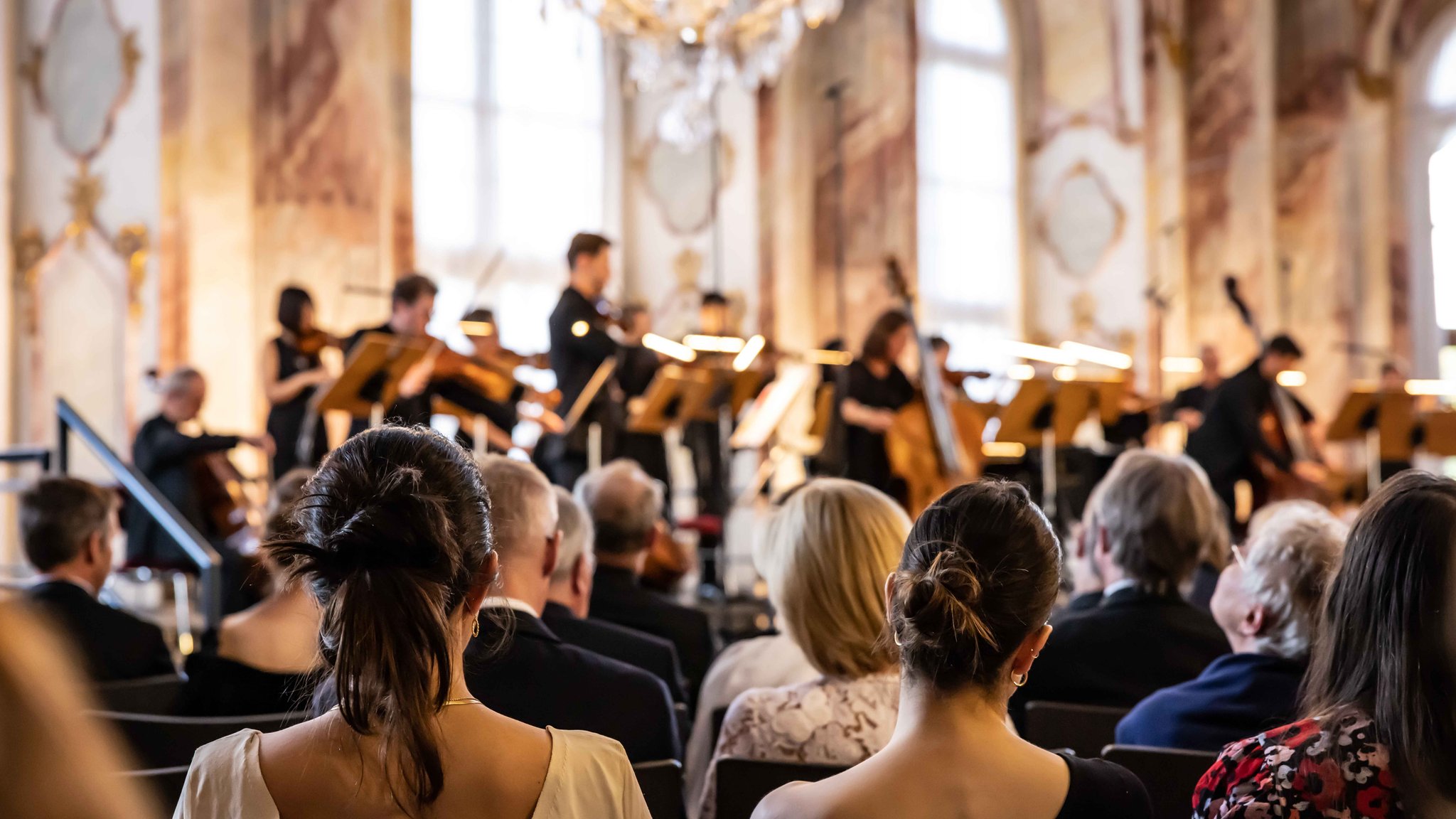 Vorne Zuschauerinnen, im Hintergrund Musikerinnen und Musiker auf der Bühne im Kaisersaal der Residenz in Würzburg.