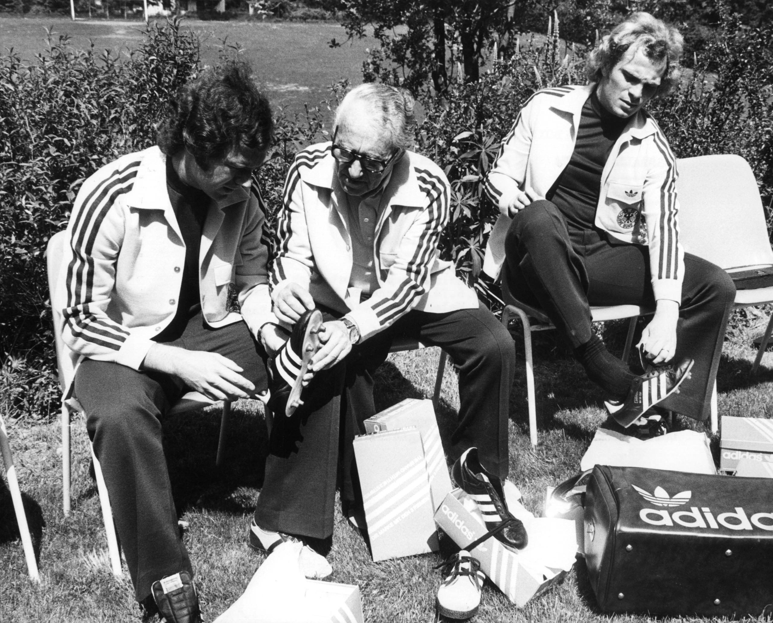 ARCHIV - 30.05.1974, Schleswig-Holstein, Malente: Libero und Kapitän Franz Beckenbauer (l) und Mittelfeldspieler Uli Hoeneß (r) probieren am 30.5.1974 auf dem Gelände der Sportschule Malente (Schleswig-Holstein) neue Fußballschuhe an, die Adi Dassler mitgebracht hat. In Malente bereitet sich die deutsche Fußball-Nationalmannschaft auf das am 13.6. beginnende WM-Turnier in Deutschland vor. (zu "Nike statt Adidas ab 2027: Ausrüster-Revolution beim DFB") Foto: Werner Baum/dpa +++ dpa-Bildfunk +++