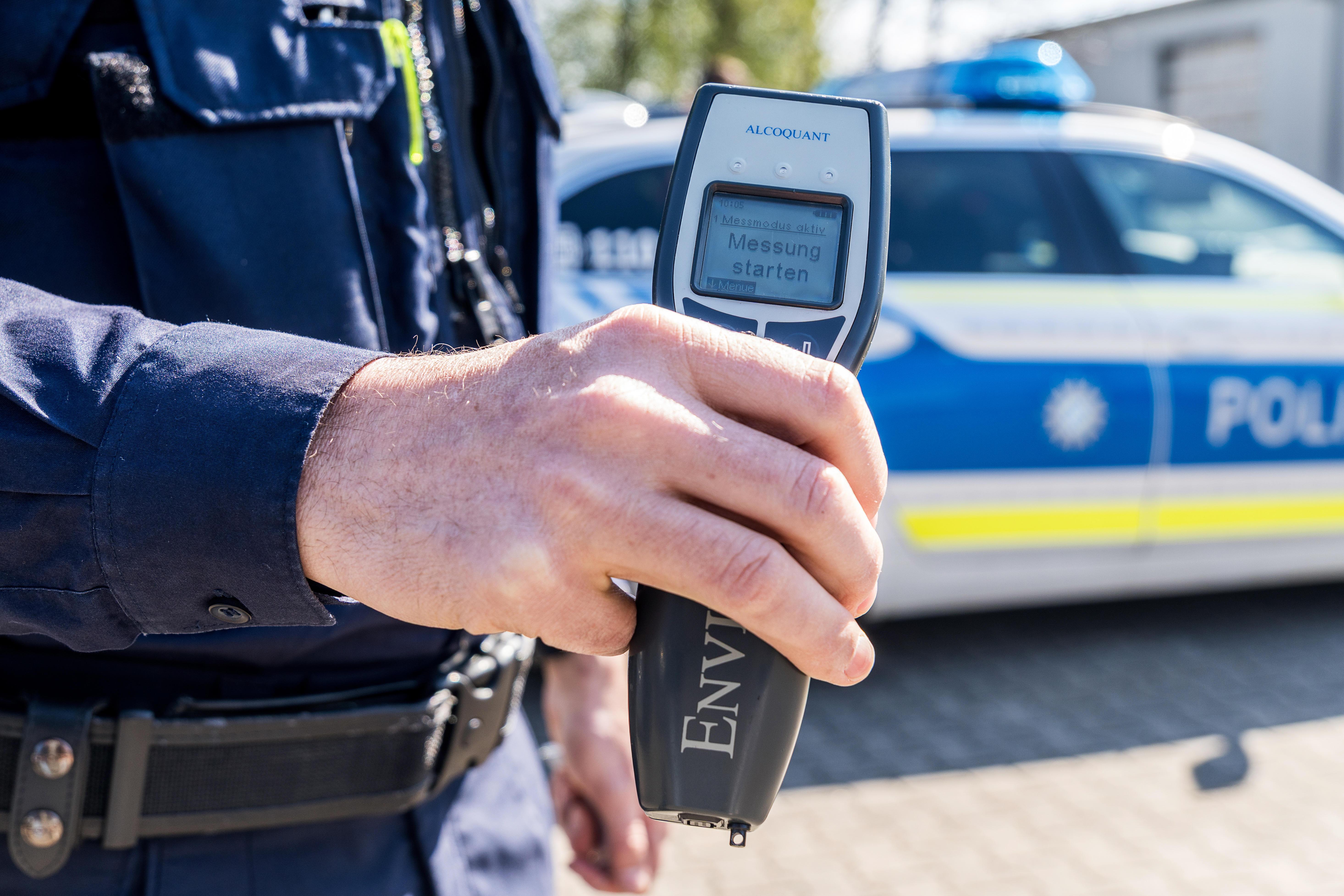 Polizist hält ein Alkoholmessgerät vor einen Streifenwagen 