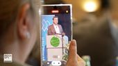 Auf dem Display eines Handys ist Ministerpräsident Markus Söder an einem Rednerpult zu sehen. | Bild:BR