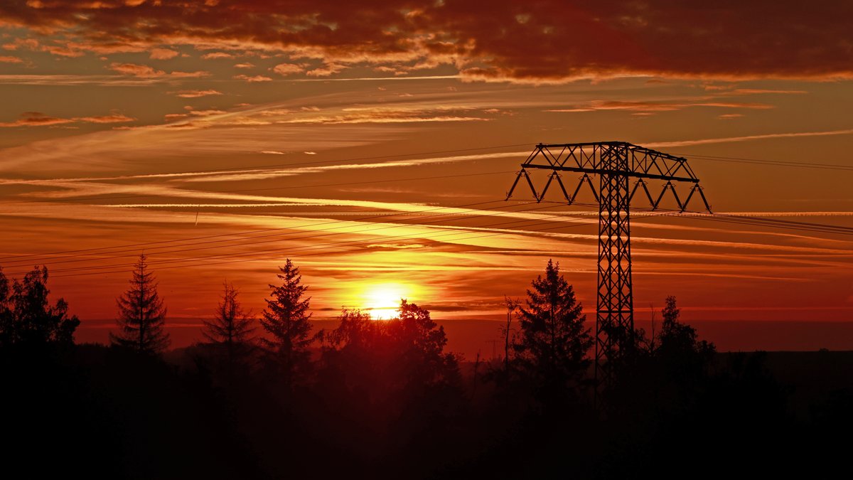Die Sonne geht hinter einer Stromtrasse im Oberharz bei Elbingerode auf.