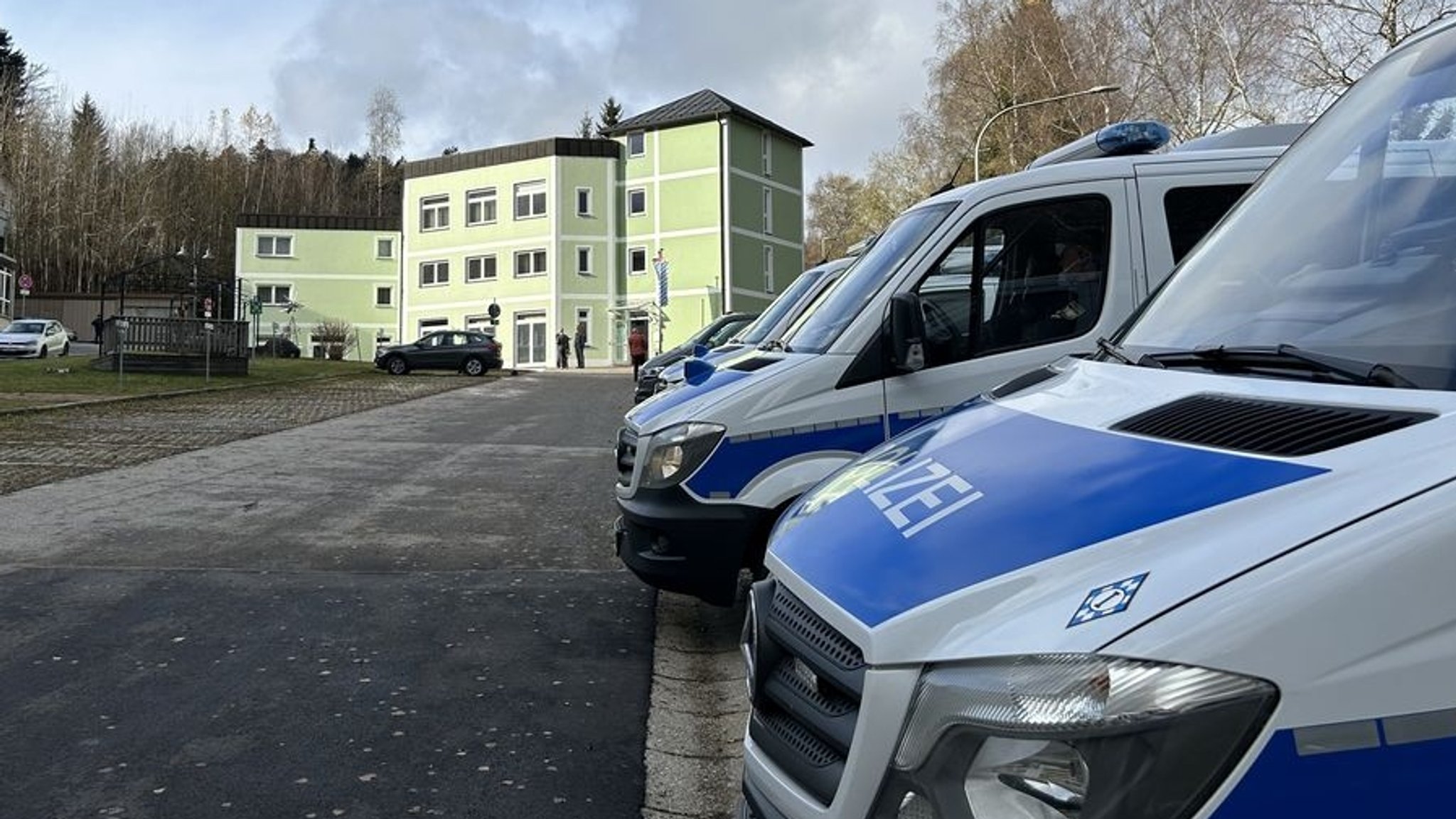 Polizeifahrzeuge stehen auf einem Parkplatz vor einem grünen Gebäude