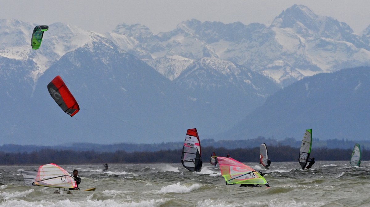 Bayern, Herrsching: Windsurfer und Kiter nutzen den starken Wind auf dem Ammersee, vor der Kulisse der noch verschneiten Berge.