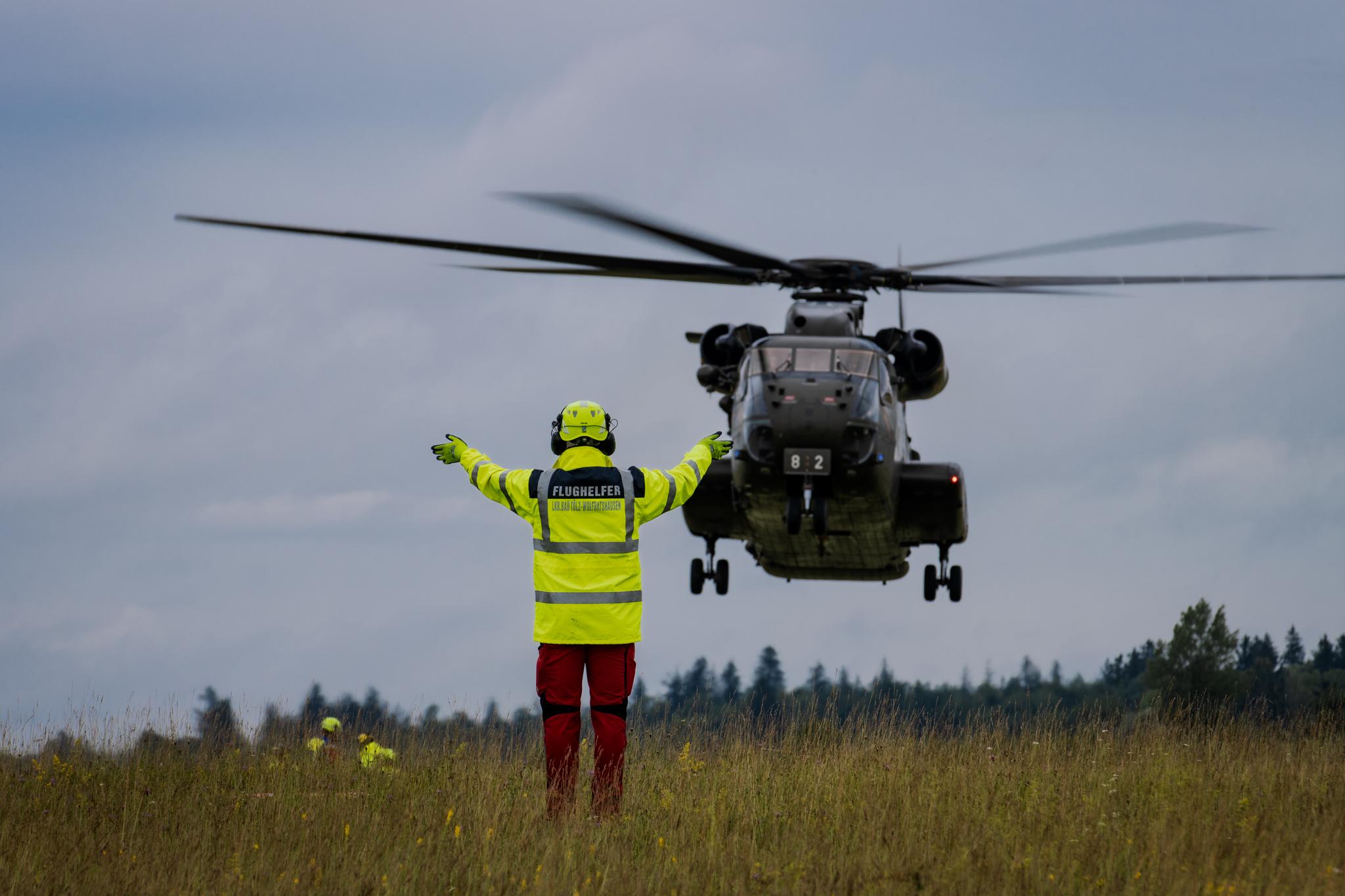 Ein Flughelfer am Boden zeigt dem Hubschrauber eine sichere Landezone an.
