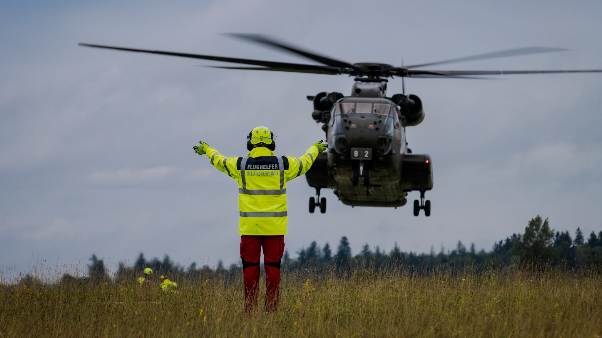 Ein Flughelfer am Boden zeigt dem Hubschrauber eine sichere Landezone an.