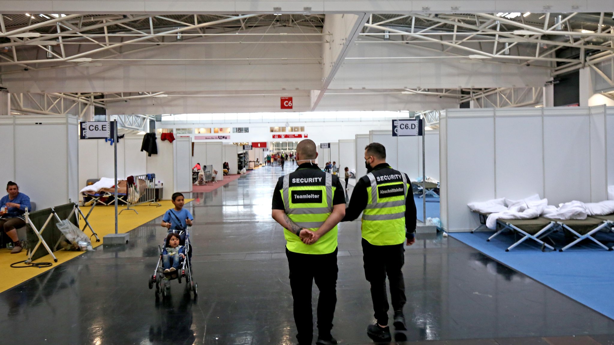 Blick in Halle C6, ein Kind schiebt ein anderes Kind im Buggy, daneben zwei Männer in Security-Westen.