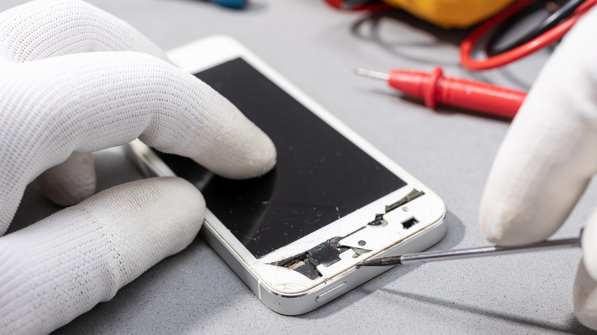 Hände, die ein kaputtes Smartphone reparieren
