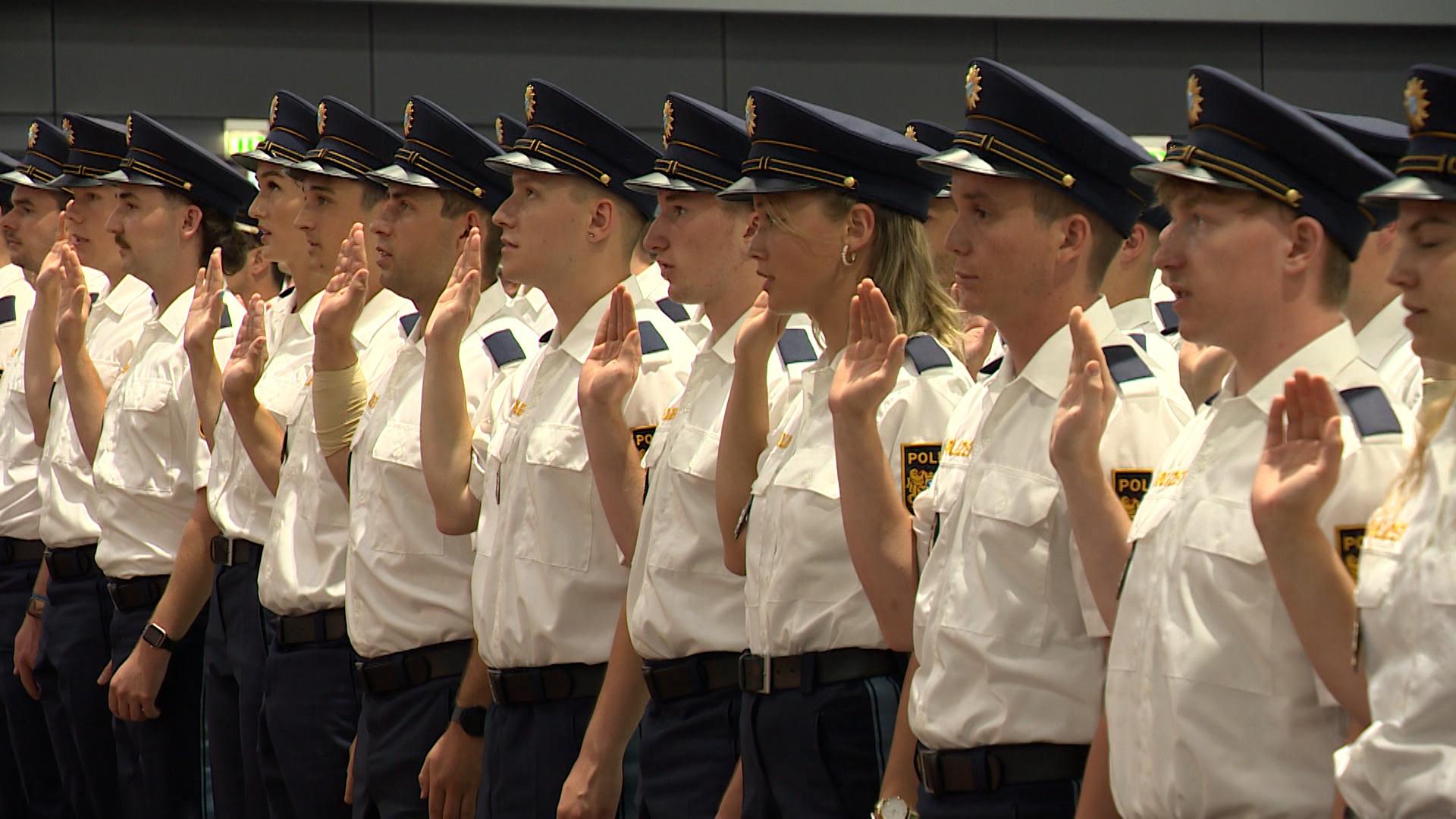 Polizistinnen und Polizisten in Uniform heben bei ihrer Vereidigung die rechte Hand.