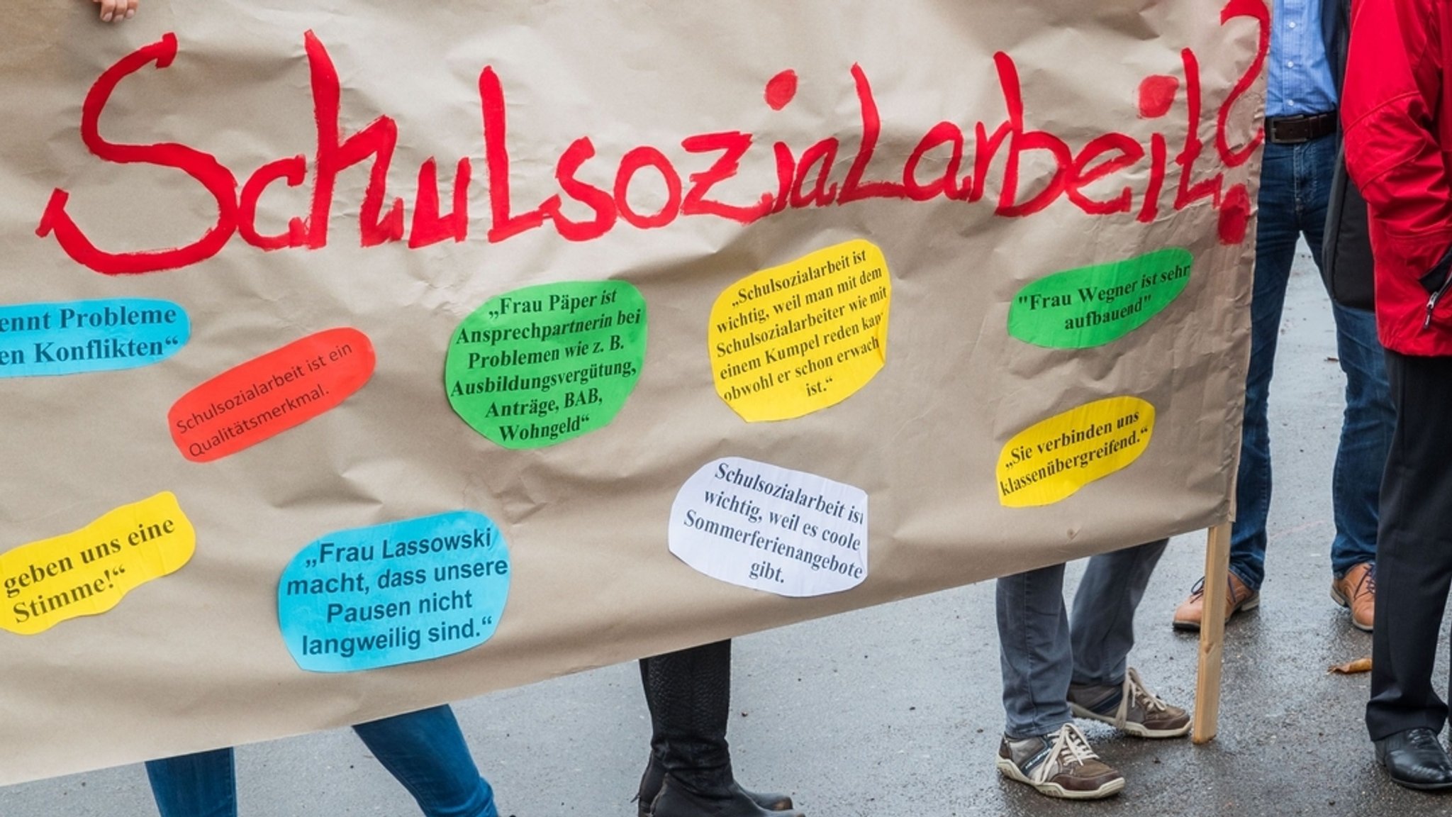 Teilnehmer einer Demonstration halten ein Plakat mit der Aufschrift "Schulsozialarbeit" hoch.