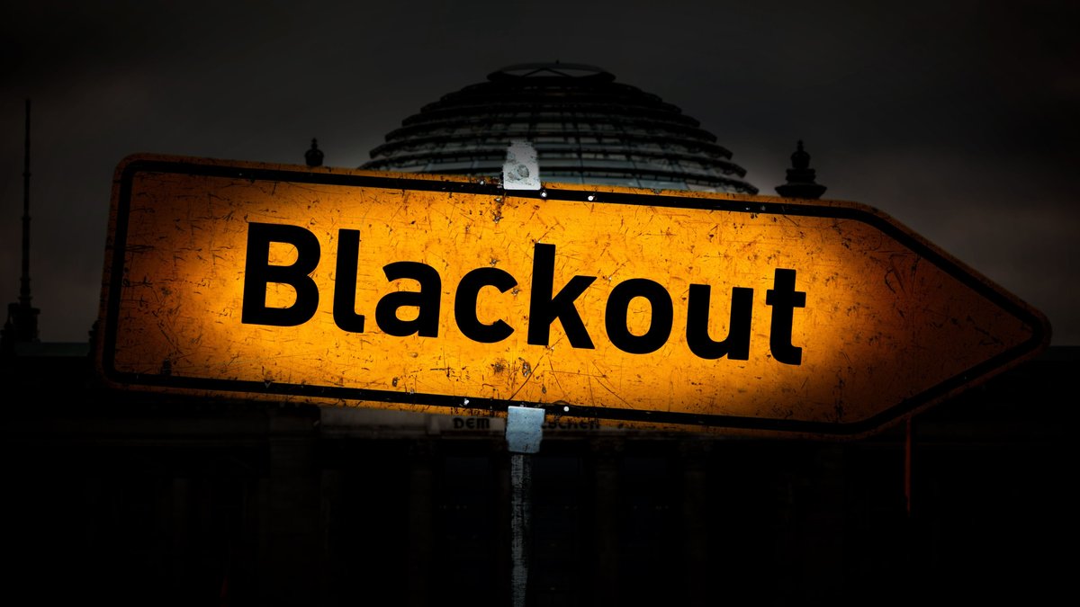 Hinweisschild mit der Aufschrift "Blackout", angeleuchtet von einem Lichtkegel vor dem dunklen Berliner Reichstagsgebäude.