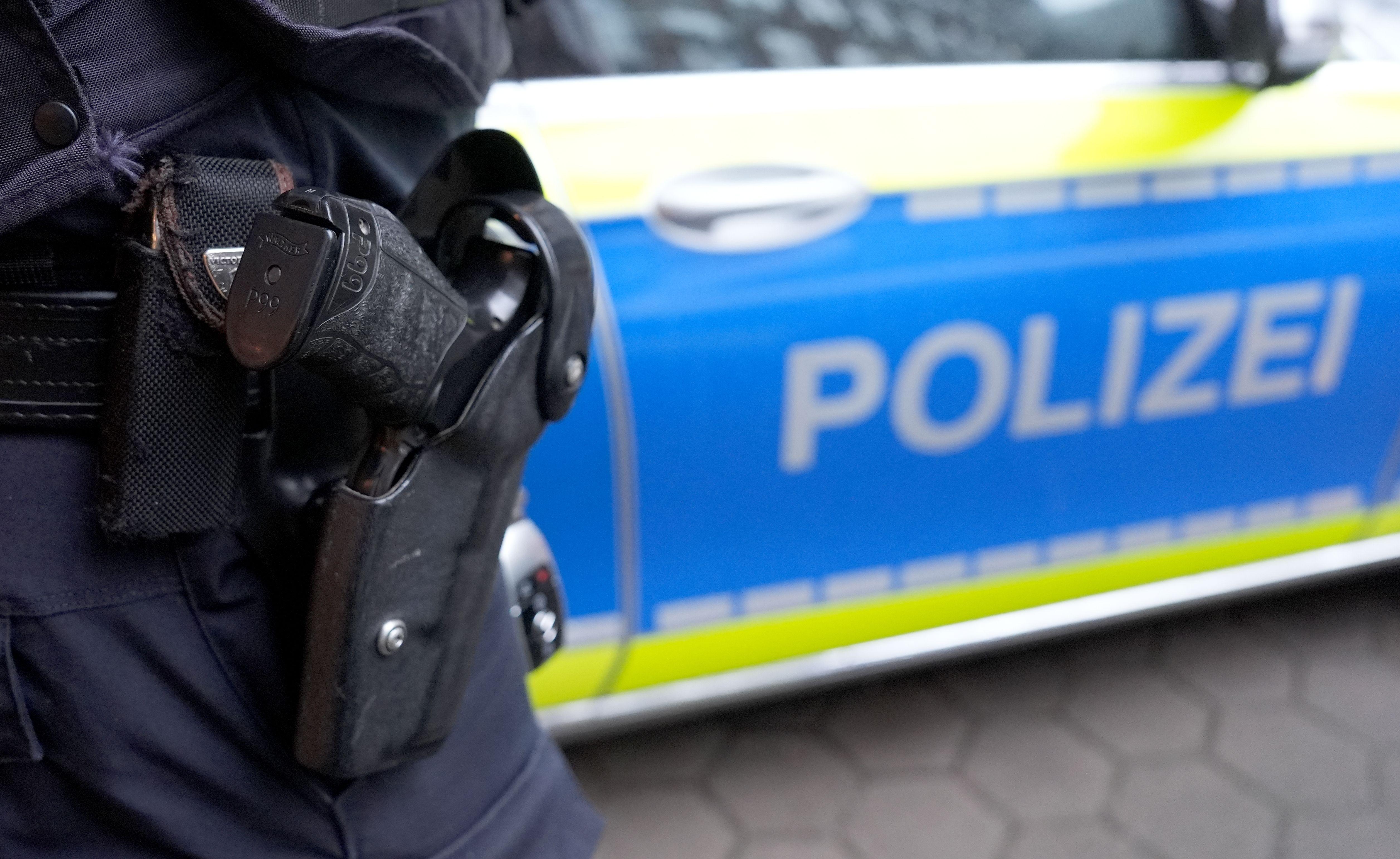 Ein Polizist mit Schusswaffe steht vor einem Einsatzfahrzeug der Polizei.
