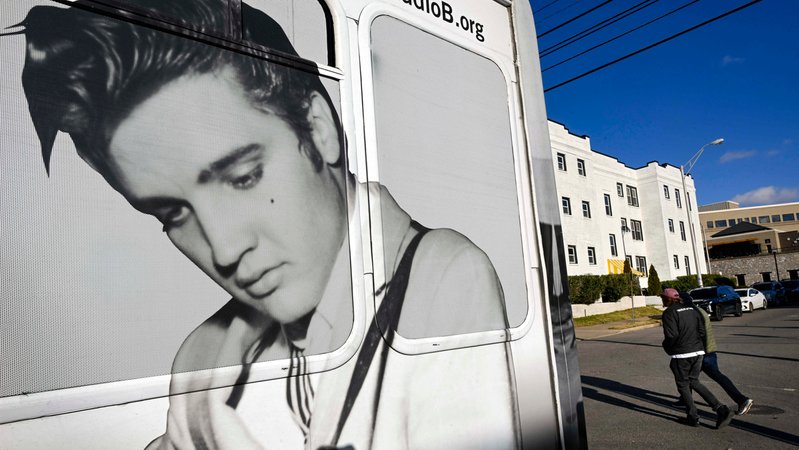 Fußgänger gehen an einem Bus vorbei, auf dem ein Bild von Elvis Presley zu sehen ist.