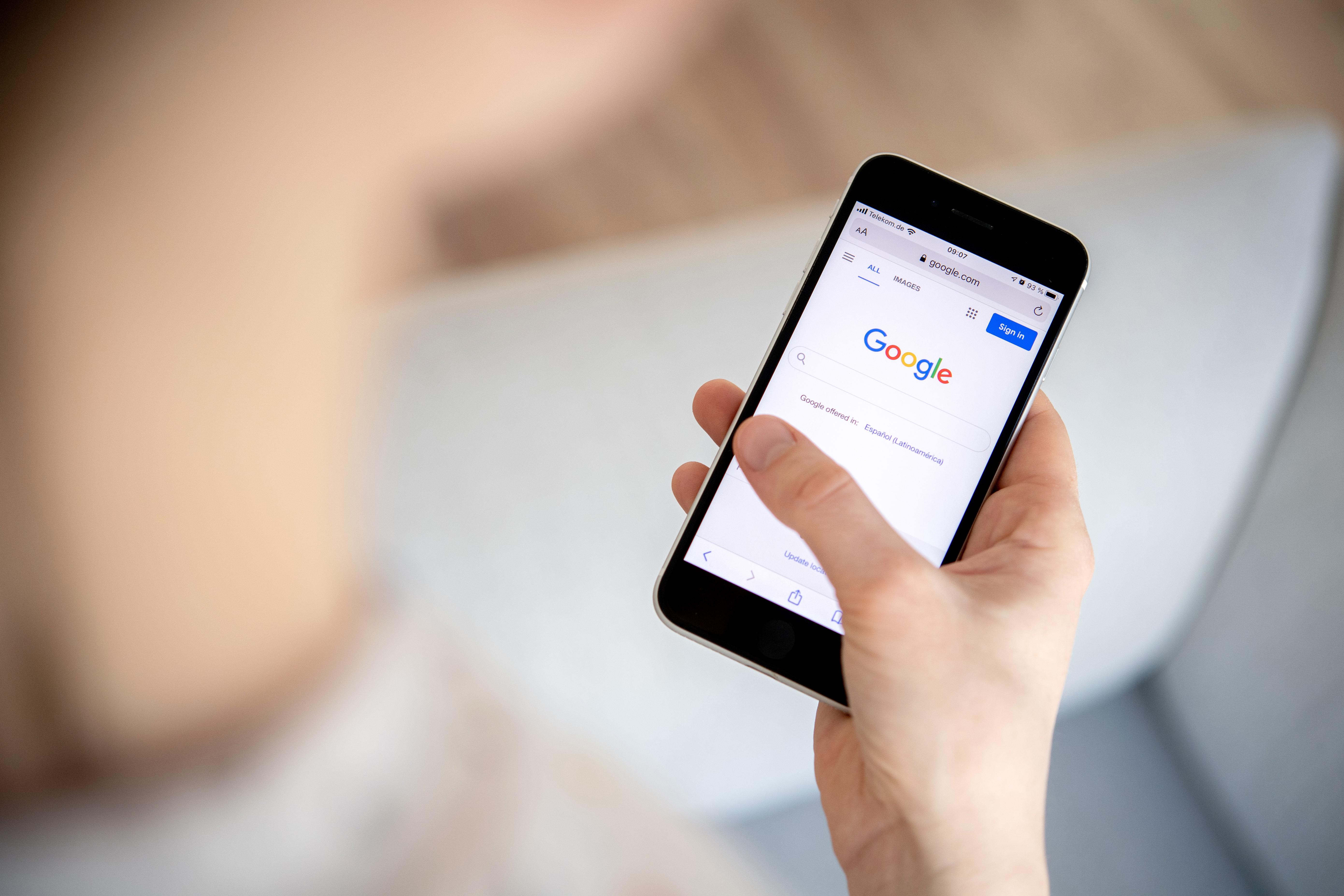 Eine Hand hält ein Handy, auf die Google-Suche angezeigt wird.