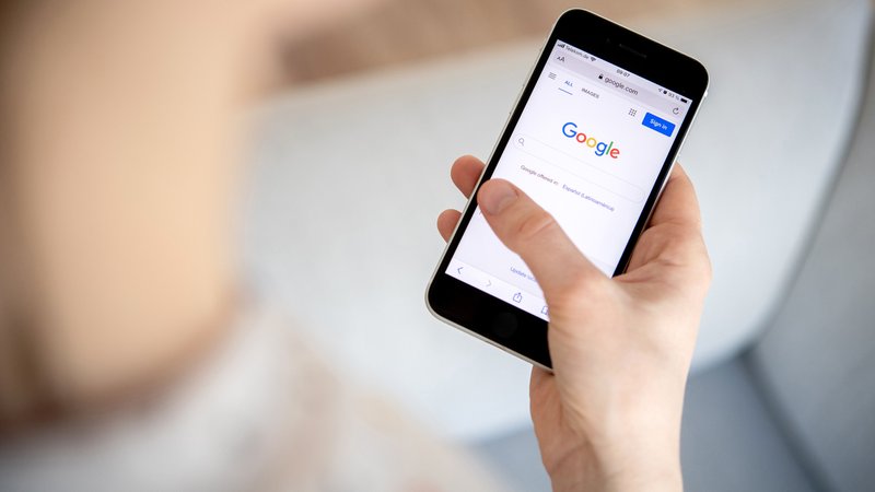Eine Hand hält ein Handy, auf die Google-Suche angezeigt wird.
