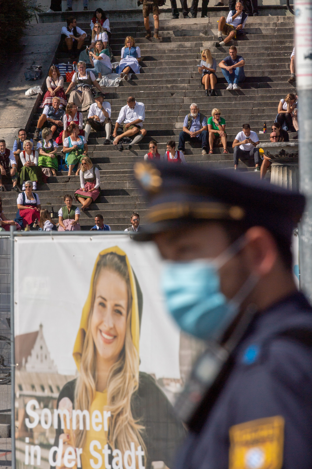 Menschen in Tracht sitzen am 19. September 2020 auf der Theresienwiese unterhalb der Bavaria. Ein Polizist trägt Mundschutz. 