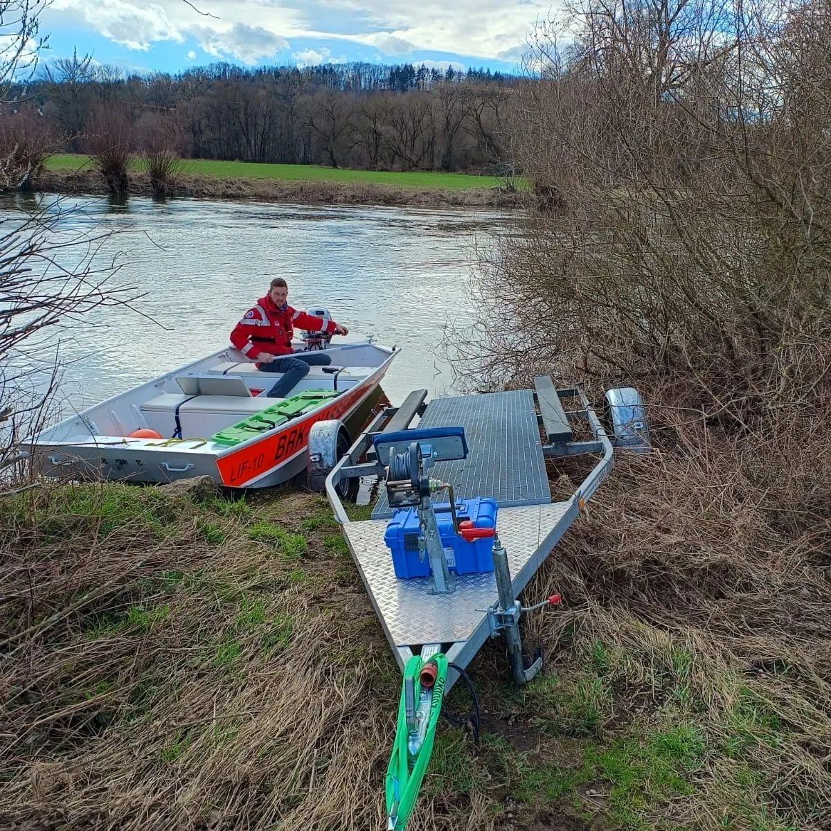 Ein Helfer der Wasserwacht Michelau sitzt in einem Rettungsboot, das auf dem Main bei Michelau im Landkreis Lichtenfels schwimmt. Am Ufer steht ein Anhänger, von dem aus das Boot zuvor ins Wasser gelassen wurde.
