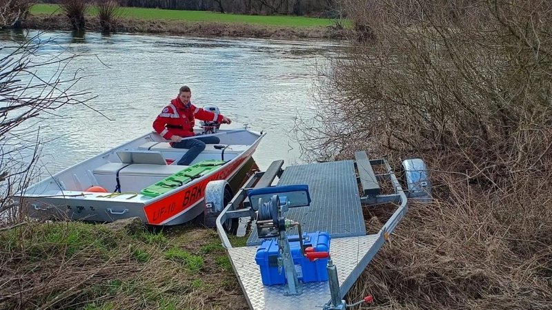 Ein Helfer der Wasserwacht Michelau sitzt in einem Rettungsboot, das auf dem Main bei Michelau im Landkreis Lichtenfels schwimmt. Am Ufer steht ein Anhänger, von dem aus das Boot zuvor ins Wasser gelassen wurde.