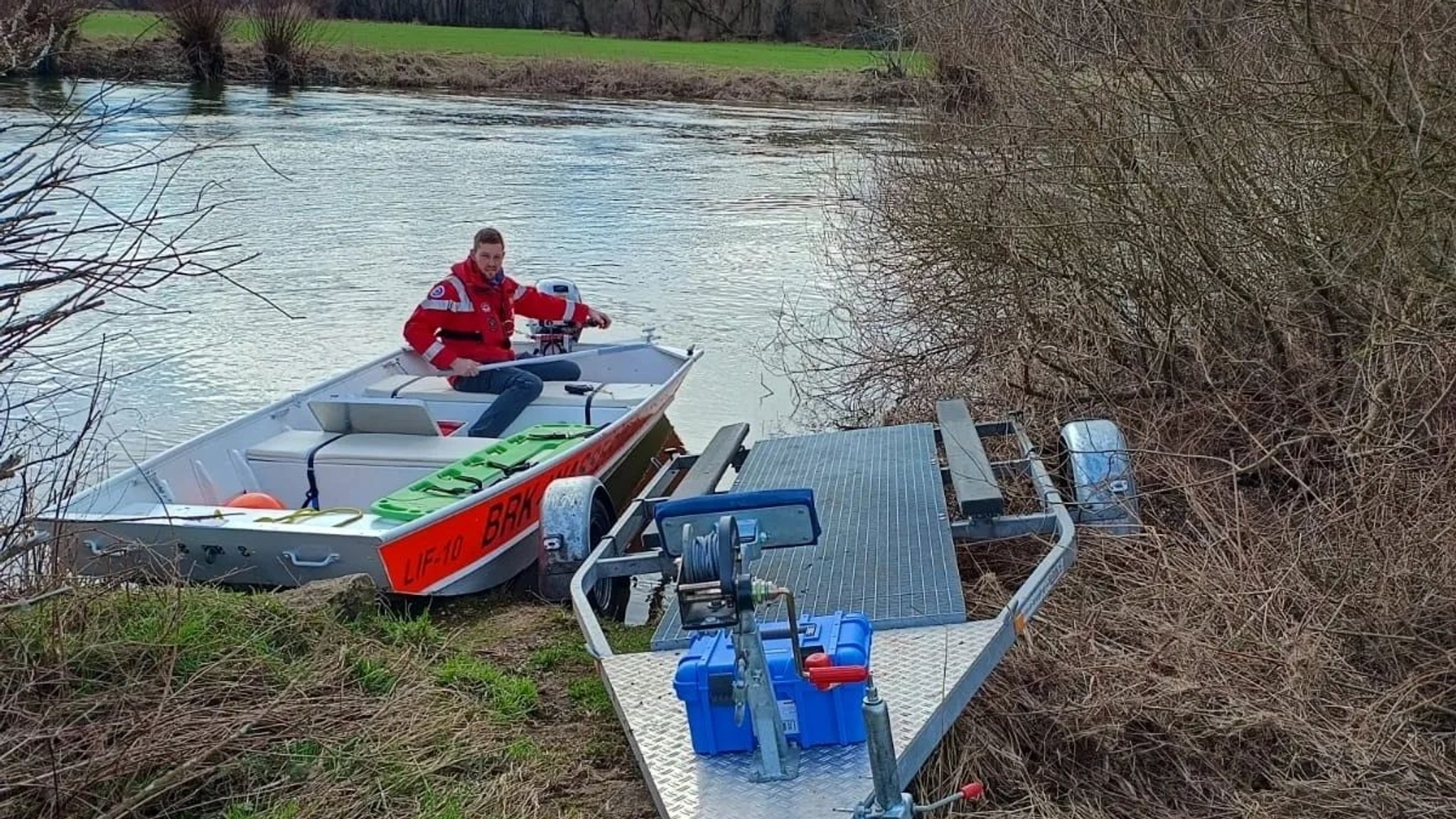 Ein Helfer der Wasserwacht Michelau sitzt in einem Rettungsboot, das auf dem Main bei Michelau im Landkreis Lichtenfels schwimmt. Am Ufer steht ein Anhänger, von dem aus das Boot zuvor ins Wasser gelassen wurde.