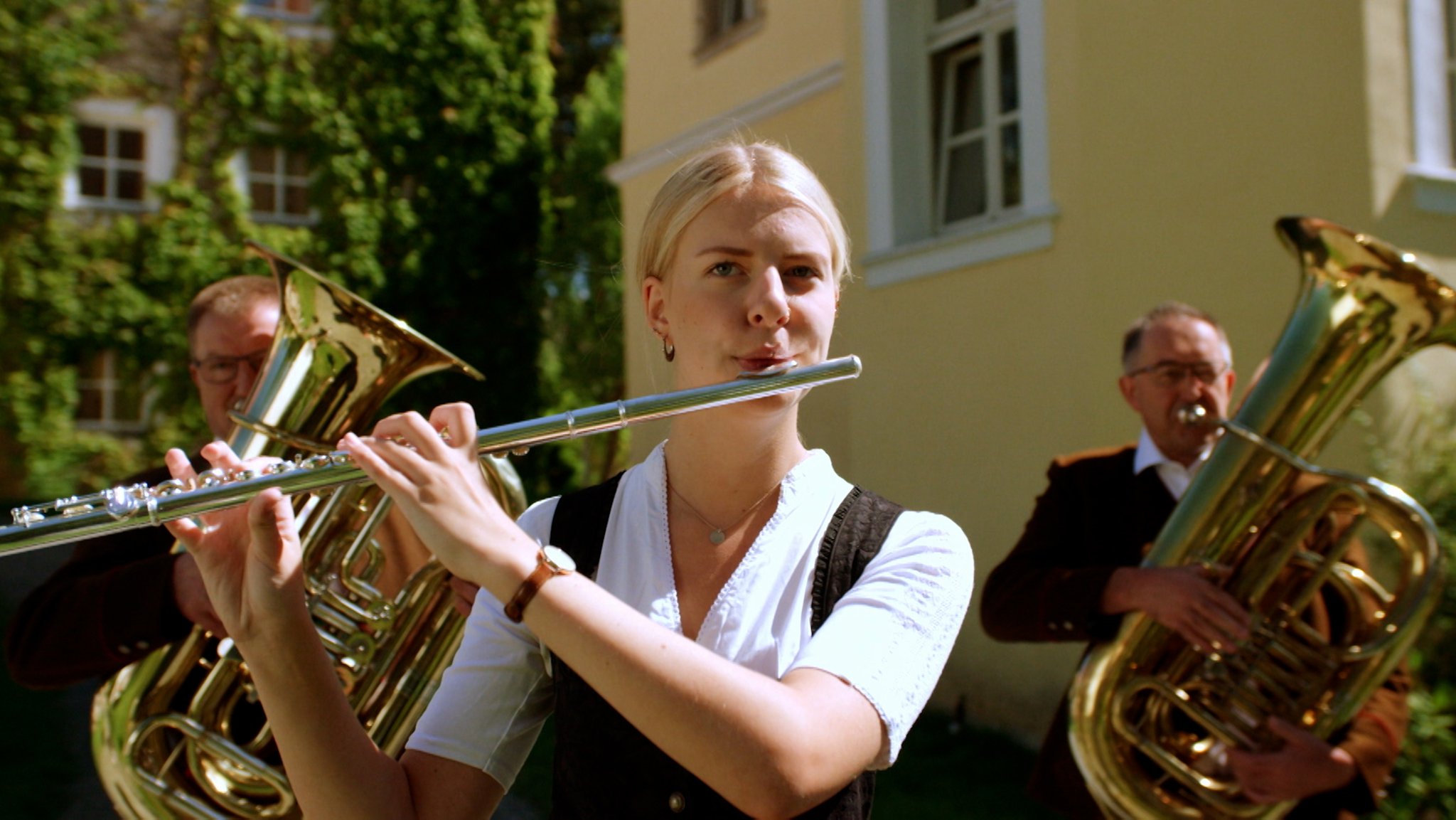 Eine Musikkapelle; in der Nahaufnahme eine Frau in Tracht, die Querflöte spielt. (Symbolbild)