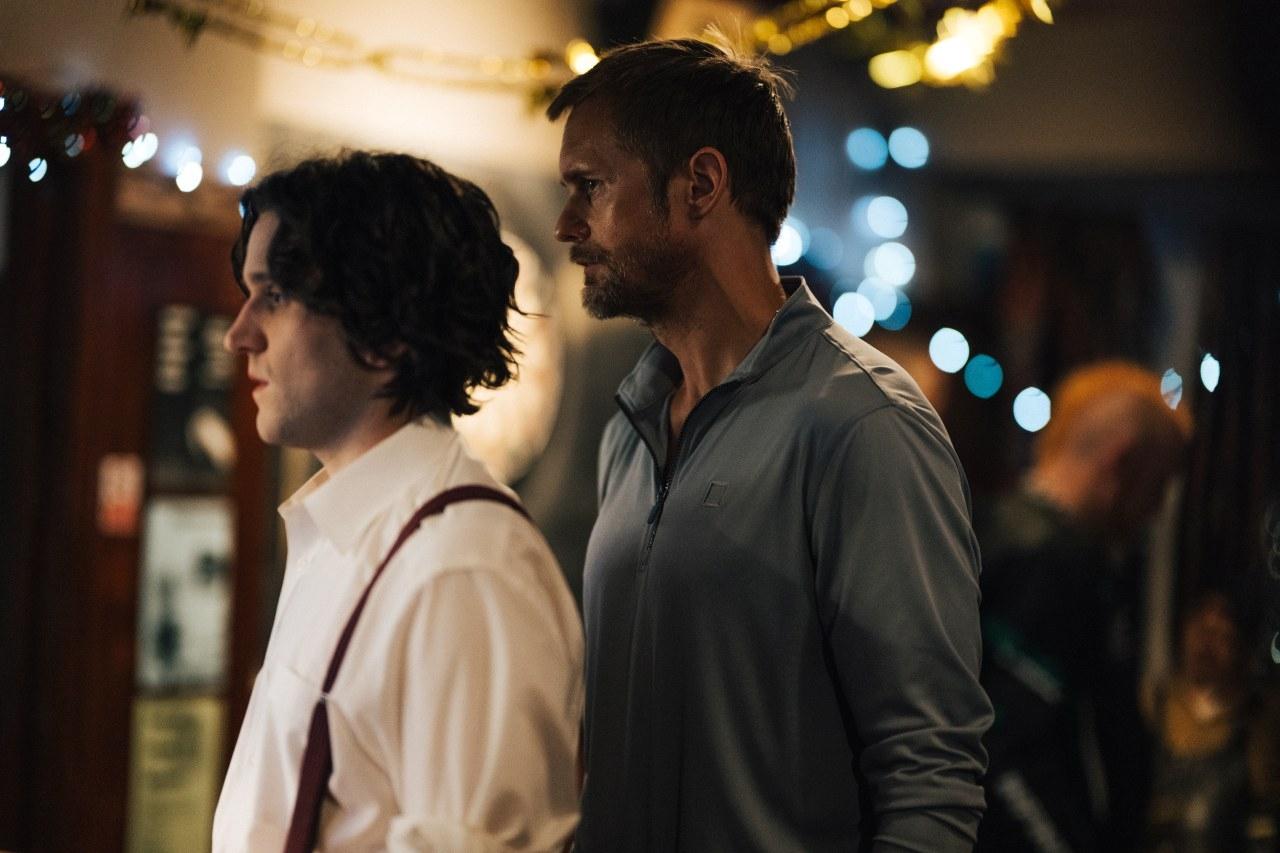 Alexander Skarsgård steht hinter Harry Melling in einer Bar-Szene aus dem Film "Pillion".
