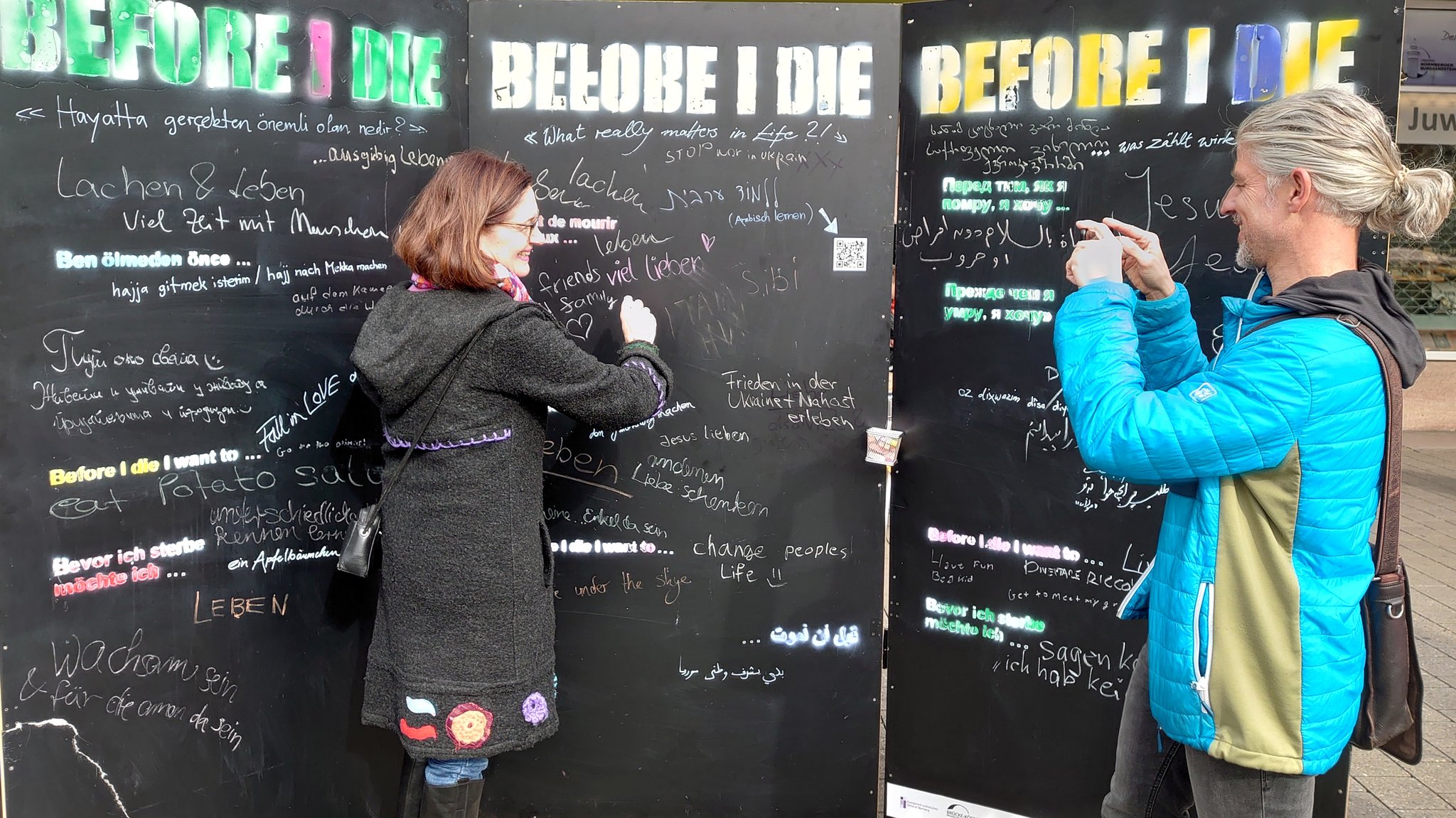 Susanne Bammessel und Thomas Amberg stehen vor drei schwarzen Tafeln der Kunstaktion "Before I die".