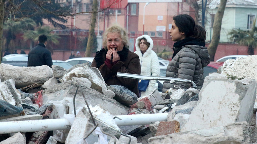 Verzweifelte Menschen stehen nach den schweren Erdbeben vor einem Trümmerhaufen.