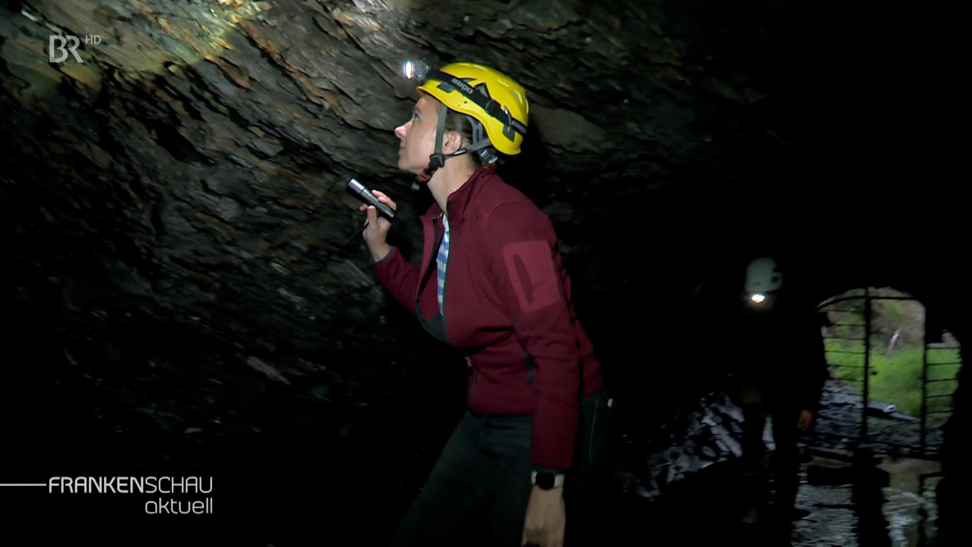 Frau mit Stirnlampe in einer Höhle.