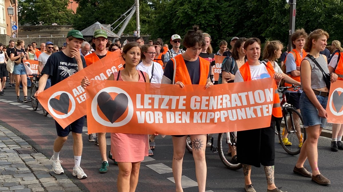 Aktivisten der Letzten Generation ziehen in einem Protestmarsch durch Bamberg. "Letzte Generation vor den Kippunkten" steht auf einem Banner.