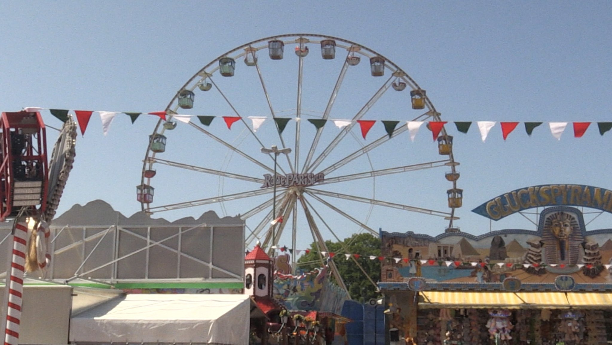 Das Riesenrad ragt auf hinter Buden wie der Glückspyradmide und einer Fähnchengirlande in den Augsburger Farben. 