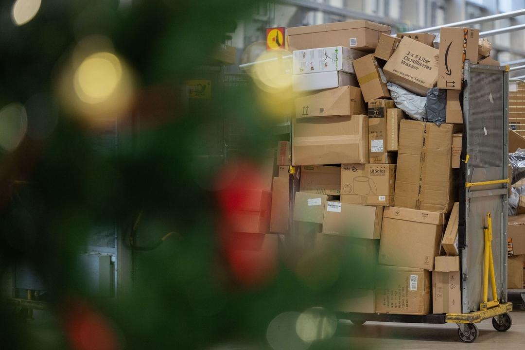 Pakete sind in einer Zustellbasis von Deutsche Post DHL hinter einem Weihnachtsbaum zu sehen.