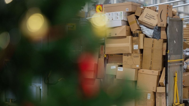 Pakete sind in einer Zustellbasis von Deutsche Post DHL hinter einem Weihnachtsbaum zu sehen. | Bild: dpa-Bildfunk/Rolf Vennenbernd Pakete sind in einer Zustellbasis von Deutsche Post DHL hinter einem Weihnachtsbaum zu sehen.