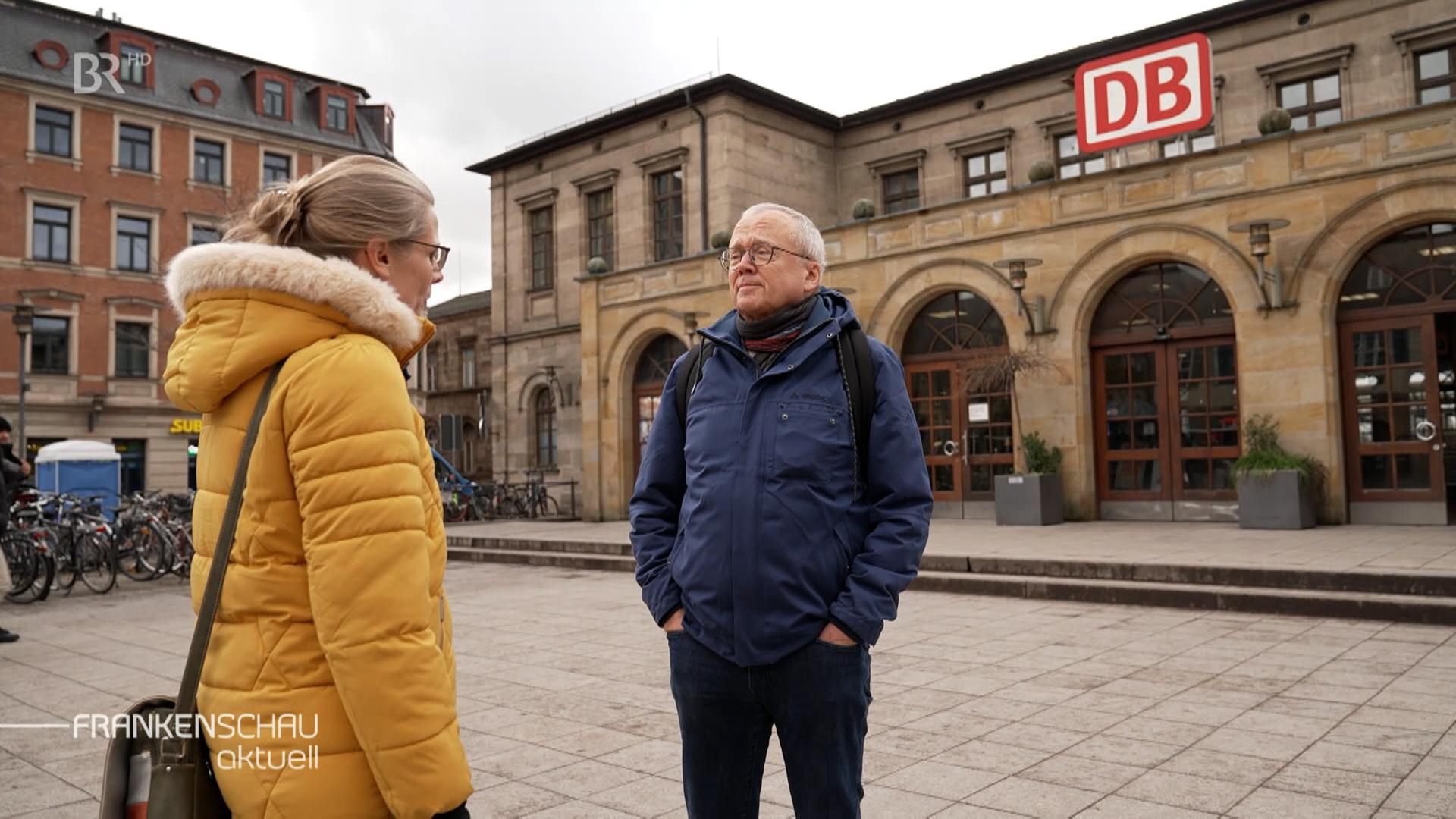 Eine Frau und Siegfried Lemmer vom Fahrgastverband "Pro Bahn" stehen auf einem leeren Bahnhofsvorplatz. 