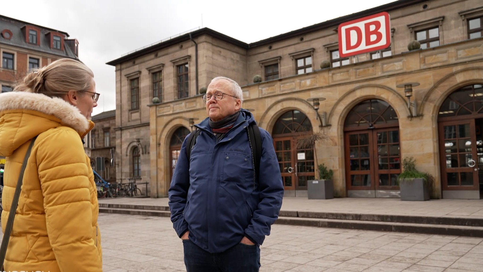 Eine Frau und Siegfried Lemmer vom Fahrgastverband "Pro Bahn" stehen auf einem leeren Bahnhofsvorplatz. 