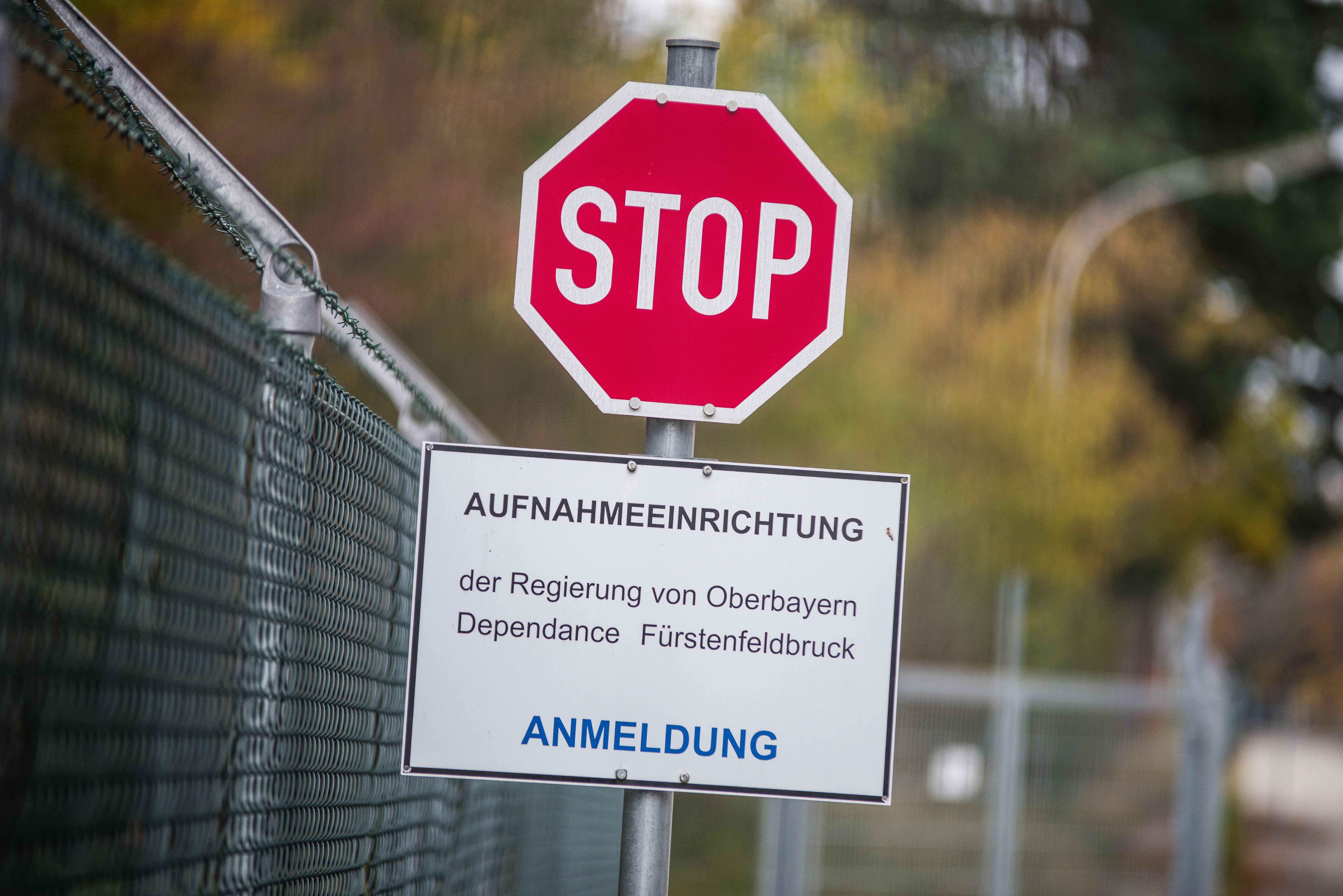 Nahaufnahme eines Stoppschilds, darunter ein Hinweisschild mit dem Text: "Aufnahmeeinrichtung der Regierung von Oberbayern Dependance Fürstenfeldbruck - Anmeldung" (Symbolbild). Was bedeutet die EU-Asylreform für oberbayerische Kommunen?