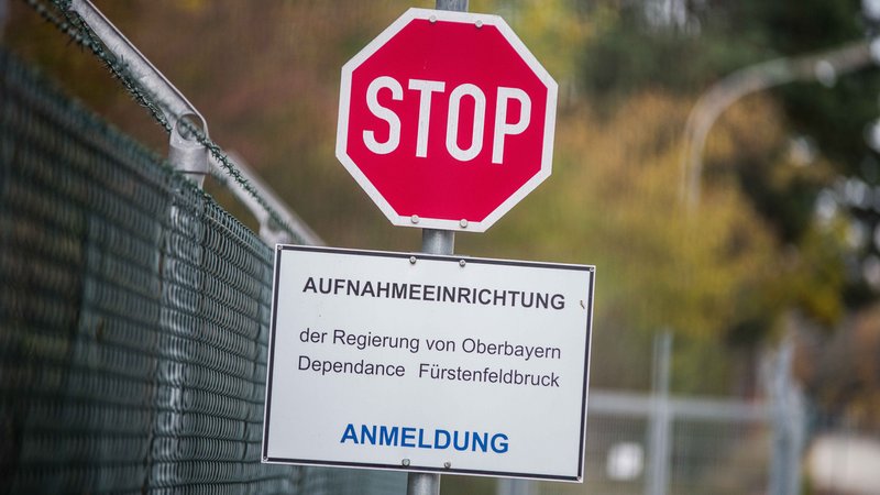 Nahaufnahme eines Stoppschilds, darunter ein Hinweisschild mit dem Text: "Aufnahmeeinrichtung der Regierung von Oberbayern Dependance Fürstenfeldbruck - Anmeldung" (Symbolbild). Was bedeutet die EU-Asylreform für oberbayerische Kommunen?