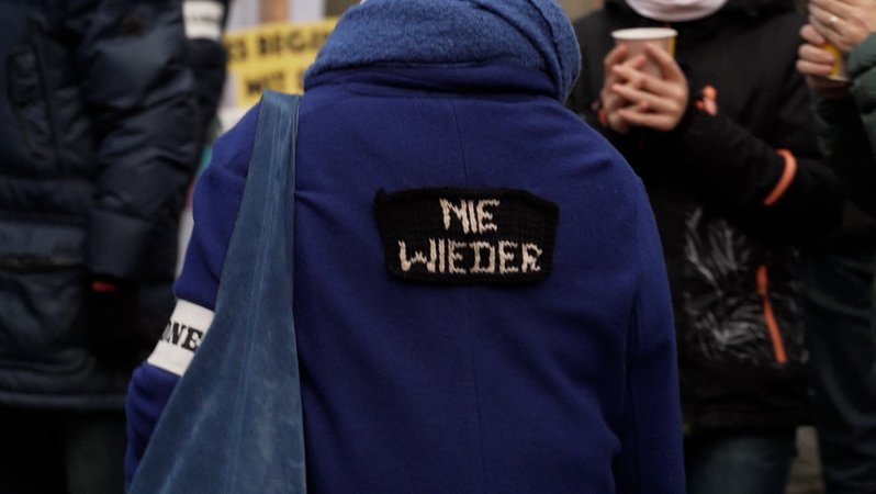 Eine Person trägt eine Jacke, auf deren Rückseite "Nie wieder" zu lesen ist. | Bild: BR24 Eine Person trägt eine Jacke, auf deren Rückseite "Nie wieder" zu lesen ist.