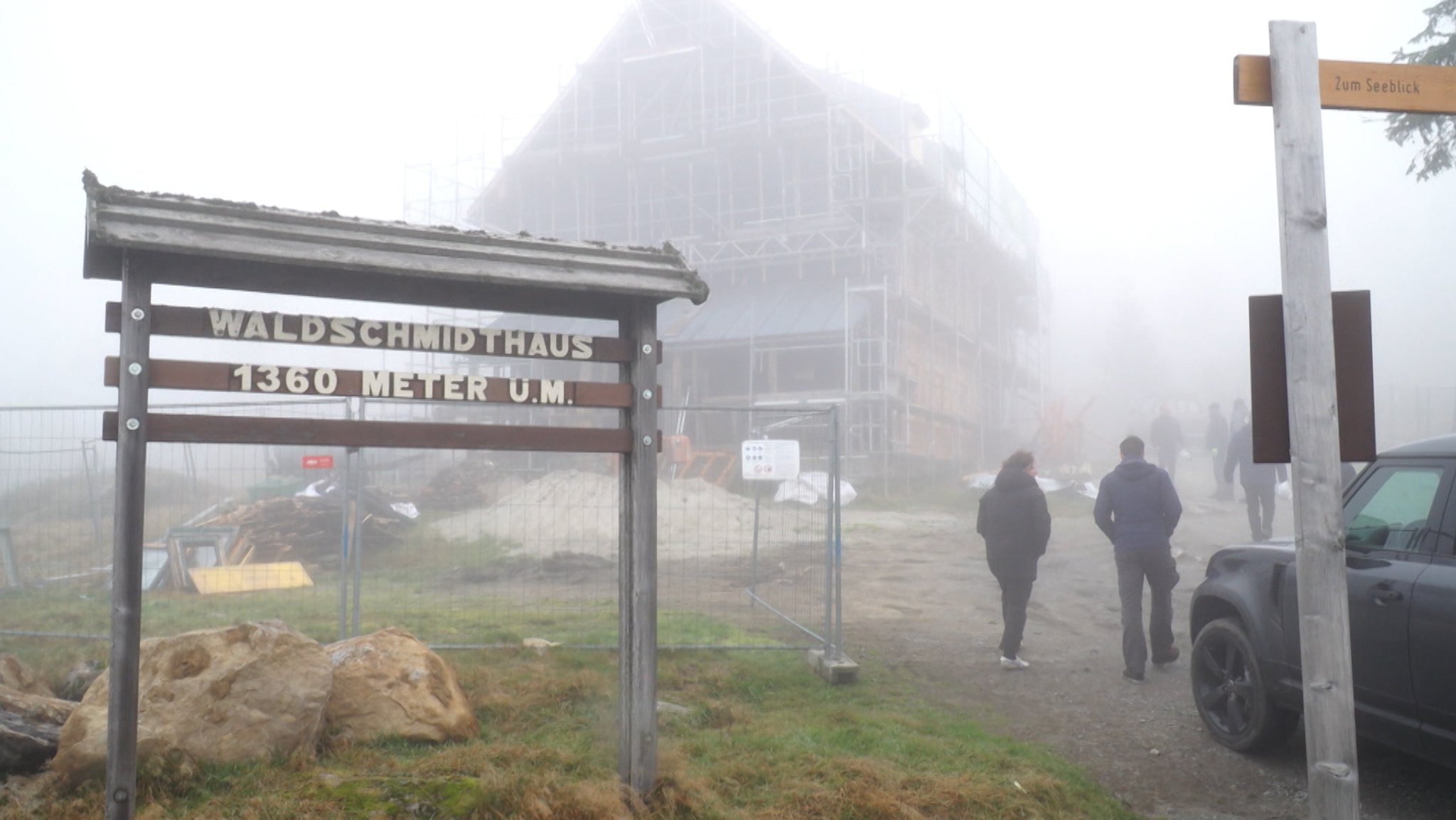 Personen laufen bei Nebel vor dem eingerüsteten Waldschmidthaus auf dem Berg Rachel.