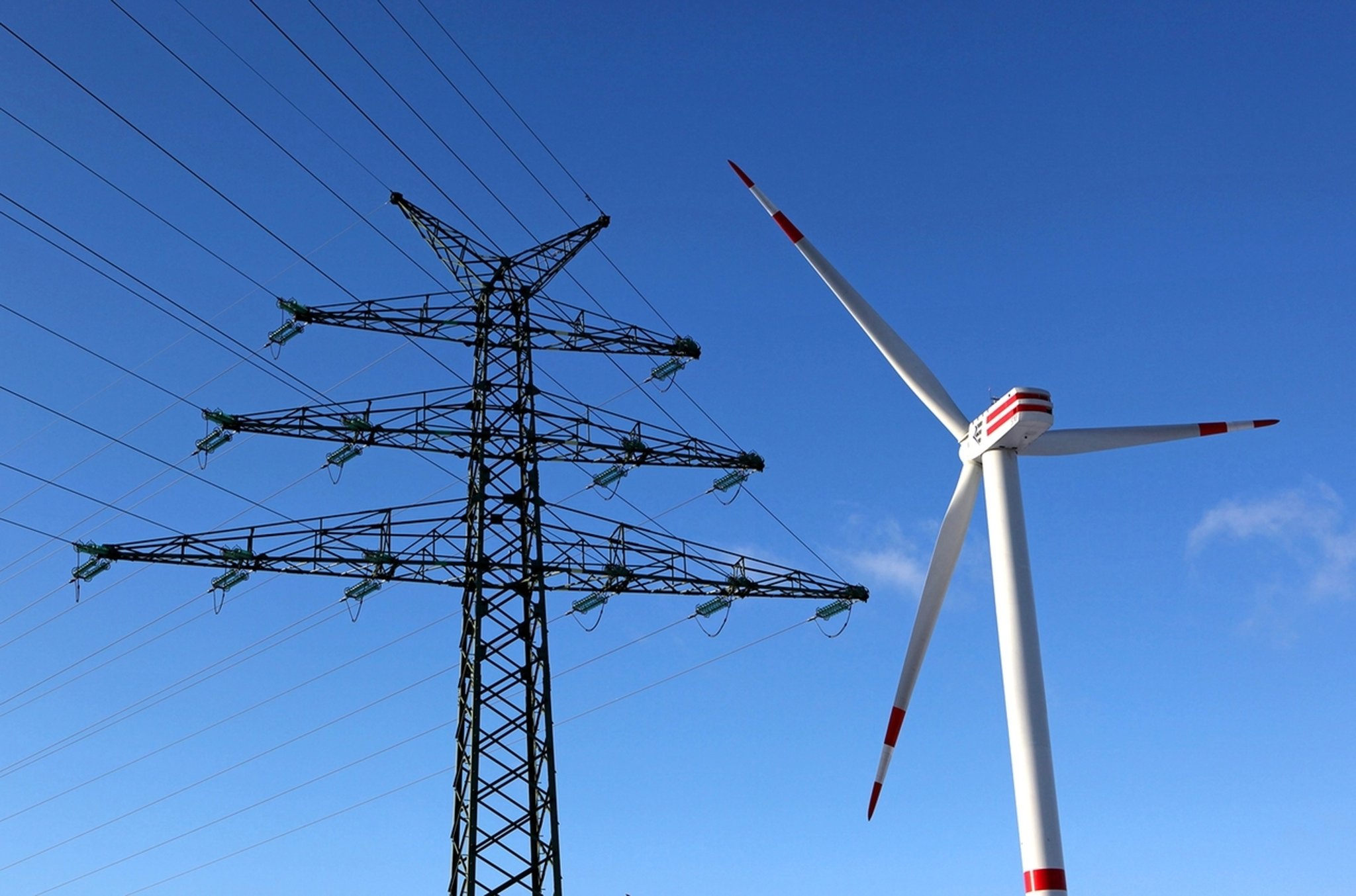 Ein Windrad neben einem Hochspannungsmast