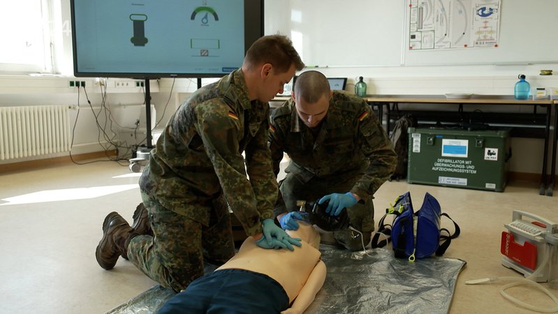 Soldaten knien neben einer Puppe. Mit deren Hilfe üben sie, einen Menschen zu reanimieren. | Bild: Kilian Neuwert/BR Soldaten knien neben einer Puppe. Mit deren Hilfe üben sie, einen Menschen zu reanimieren.