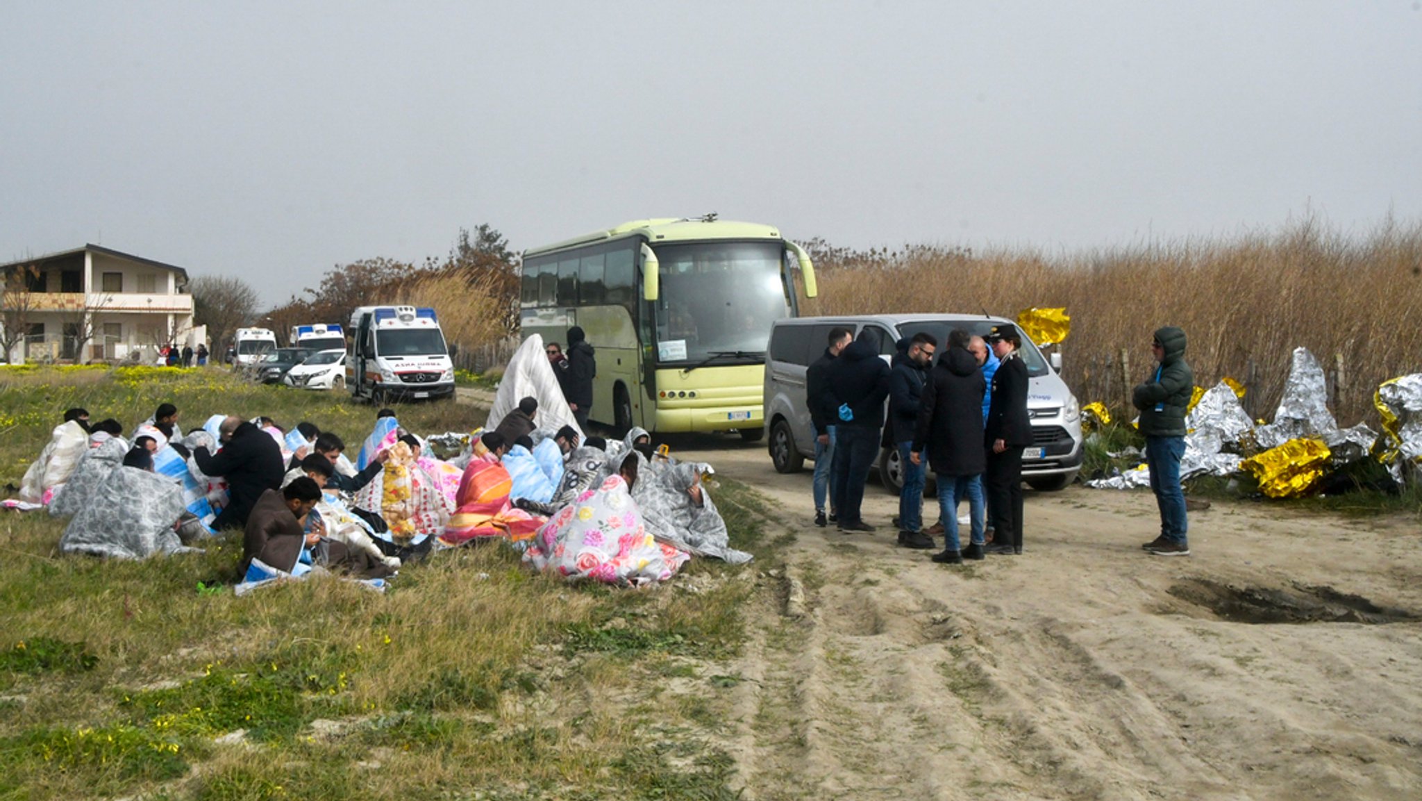 Gerettete Migranten sitzen in Decken gehüllt an einem Strand in der Nähe von Cutro. Bei einem Bootsunglück mit Migranten an der süditalienischen Küste sind Medienberichten zufolge zahlreiche Menschen ums Leben gekommen.