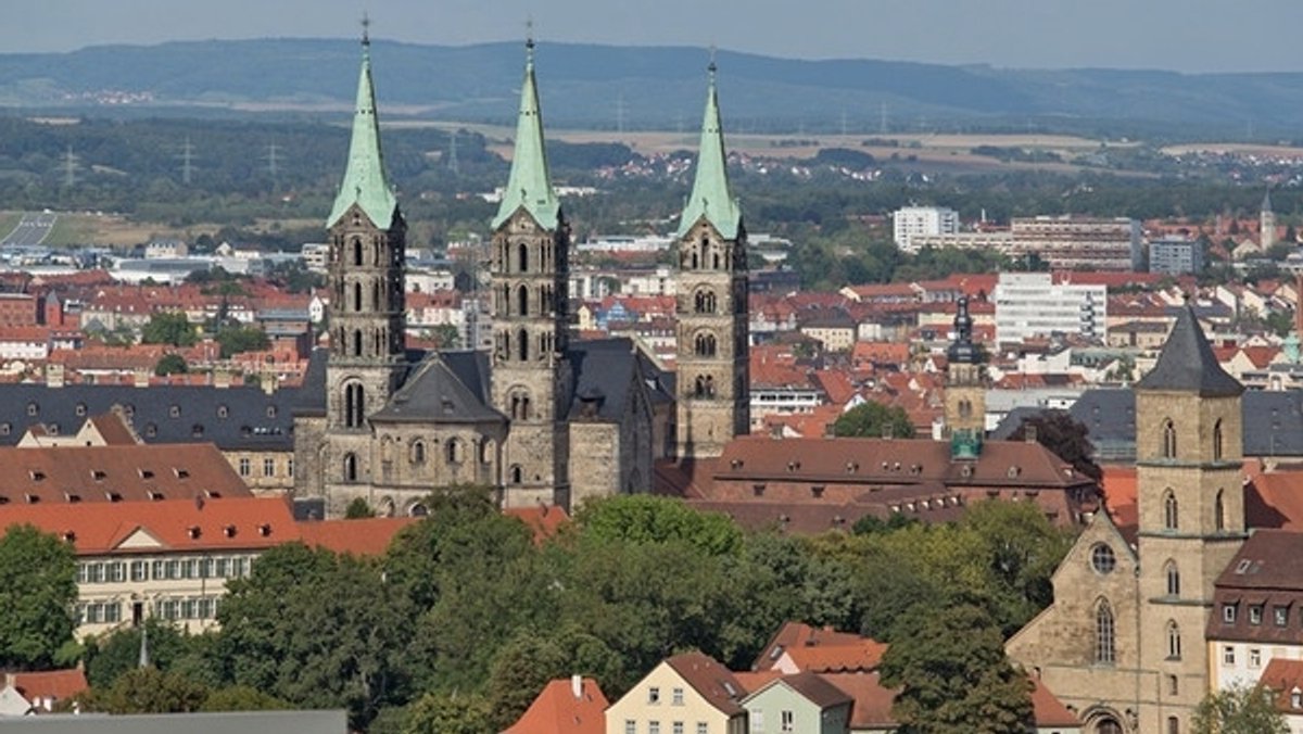 Blick aus der Vogelperspektive auf die Stadt Bamberg mit den drei Türmen des Doms, der Dachlandschaft und auch einigen Hochhäusern. 