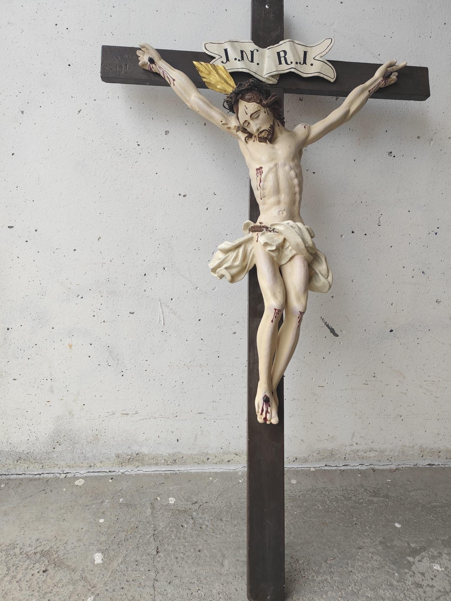 Holzkreuz mit Jesusfigur lehnt an einer Hauswand.