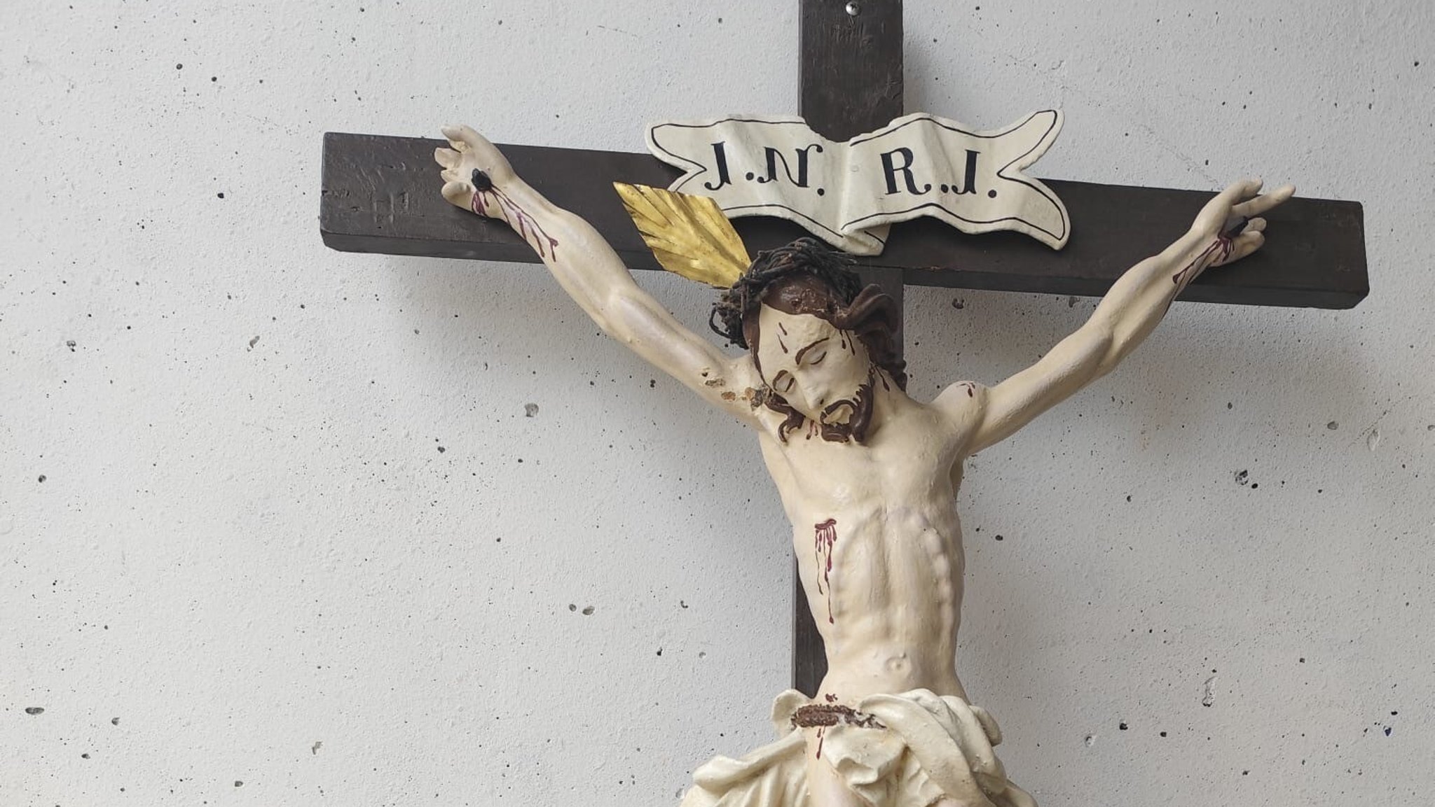 Holzkreuz mit Jesusfigur lehnt an einer Hauswand.