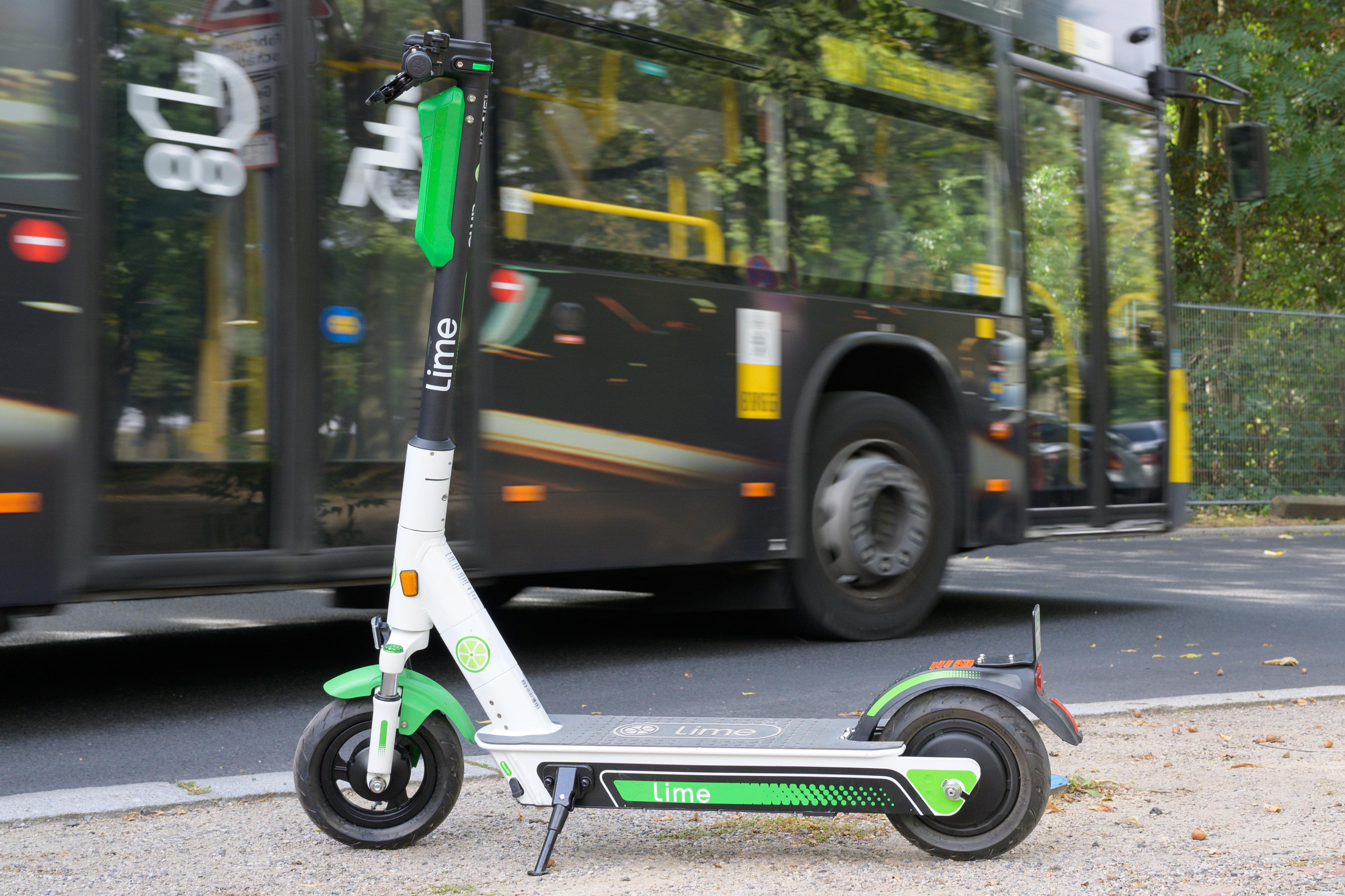 Ein E-Scooter steht auf einem Gehweg. Im Hintergrund fährt ein Bus vorbei. 